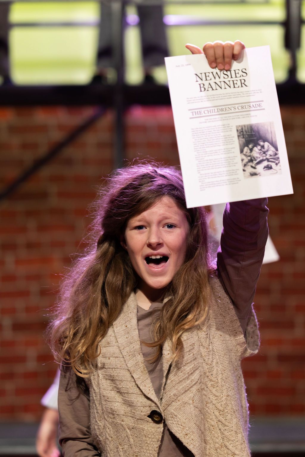 Claire House Photography event photograph of child stage performer in Newsies Jr, singing and holding a newspaper.