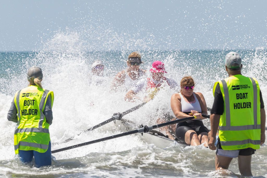 Claire House Photography event photograph of support crew assisting four beach sprint rowers as a wave splashes their boat.