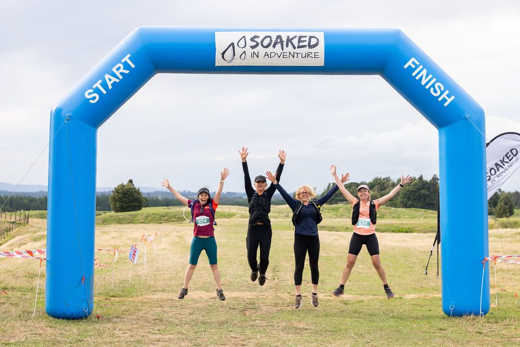 Claire House Photography event photograph of four women jumping and celebrating at the Soaked in Adventure finish line