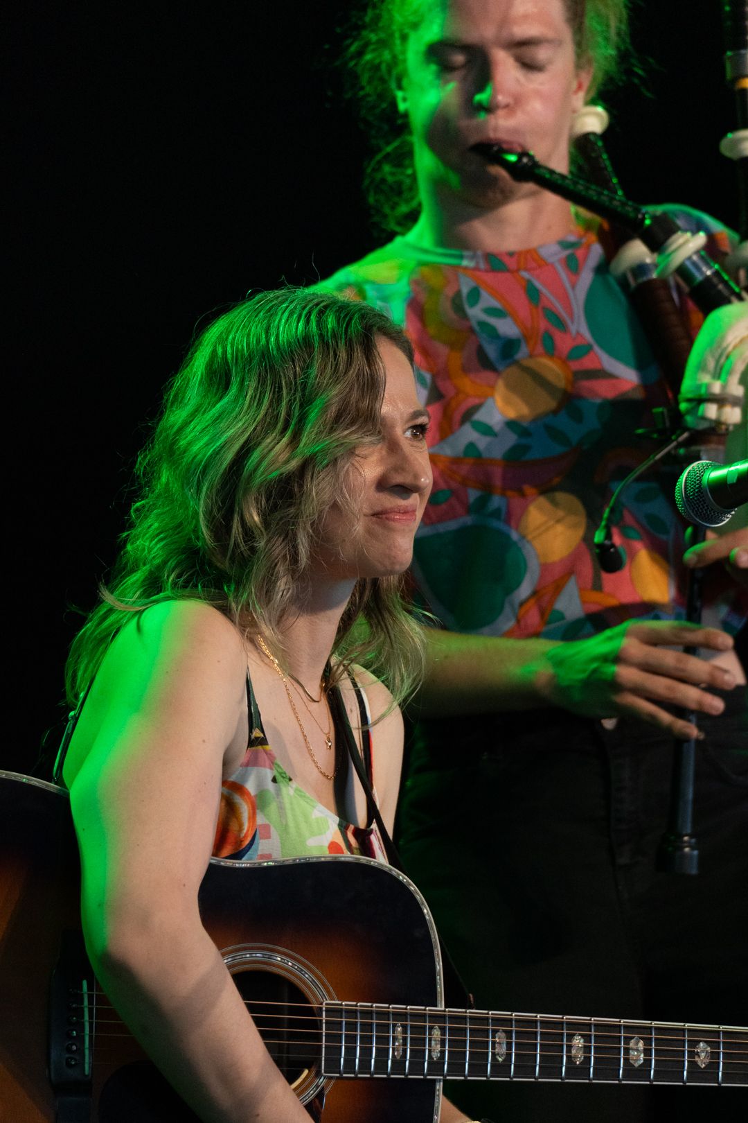 image of young woman with a guitar and a bagpiper in background