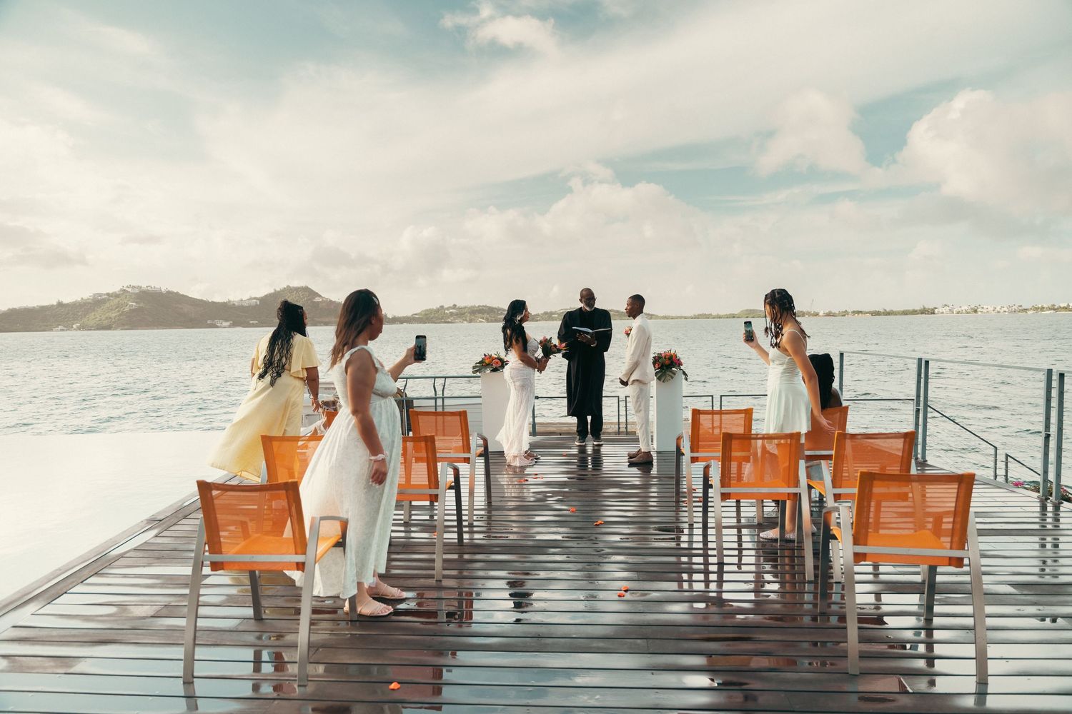 Small intimate wedding ceremony on a dock over the ocean with guests in white chairs.