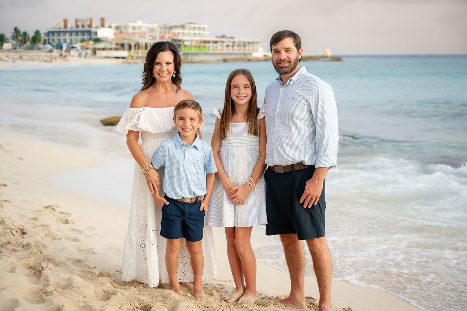 Family of four smiling on a white sand beach with ocean waves behind them.