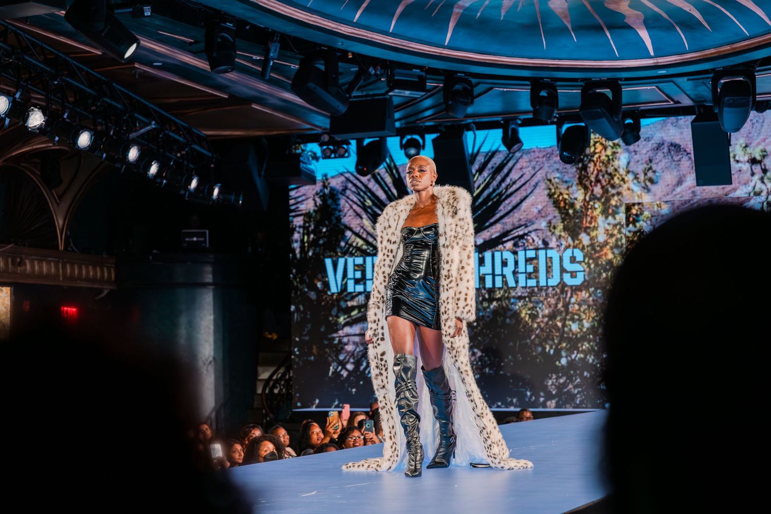 A model walks the runway in a leopard-print coat and black mini dress at a Vegas Threads fashion show.