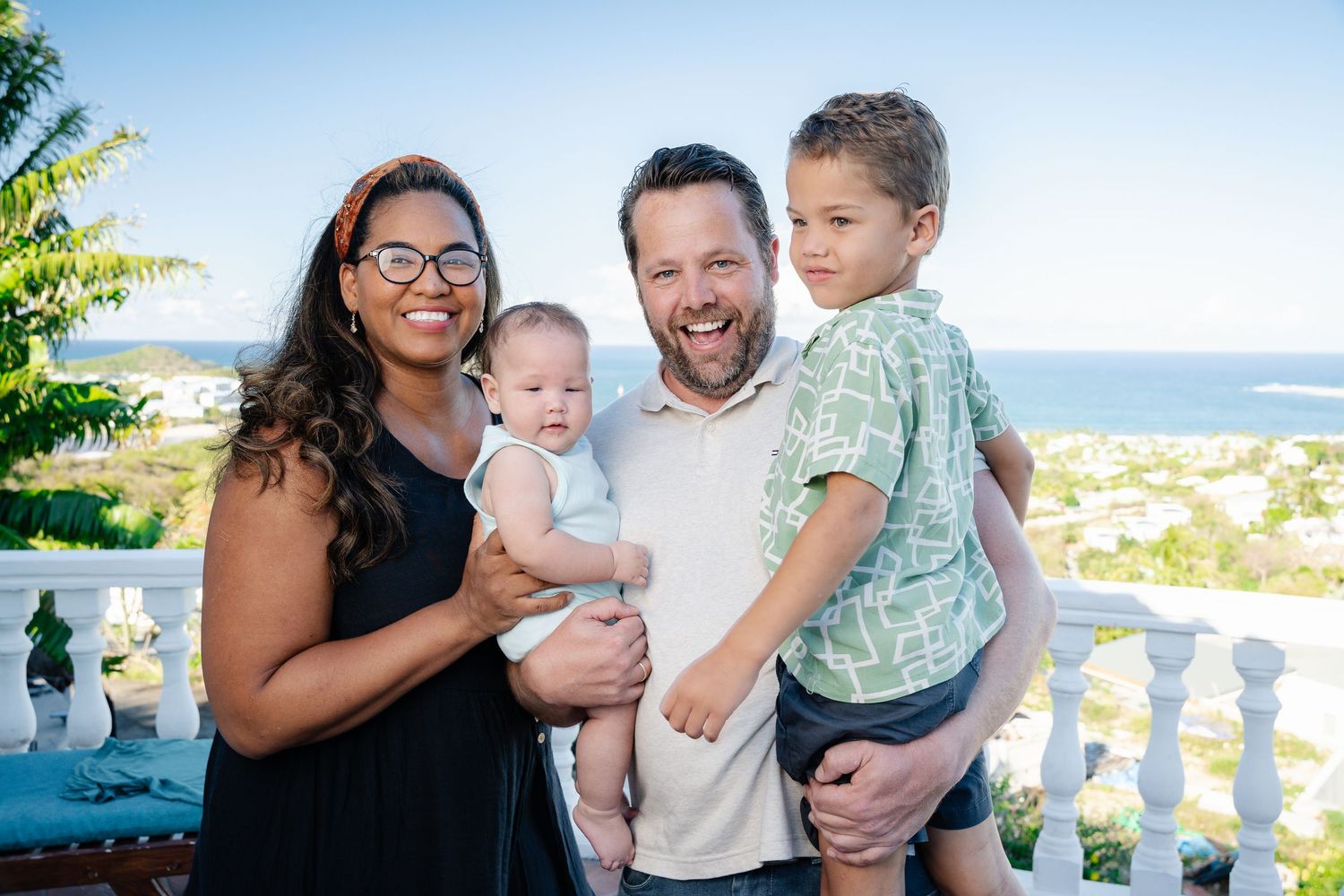 Happy family of four posing outdoors with ocean view on sunny day.