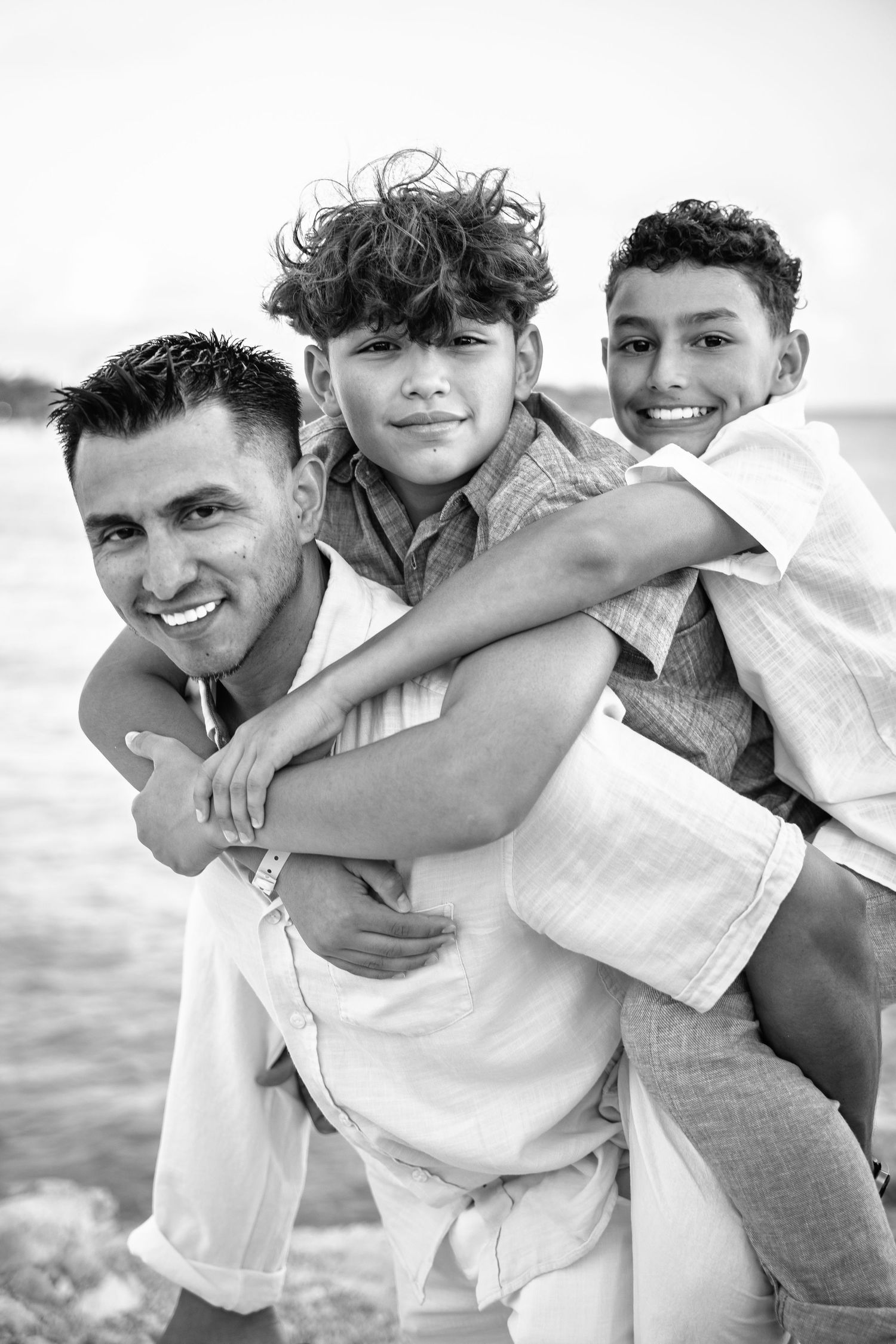 Black and white photo of father and two sons hugging at the beach.