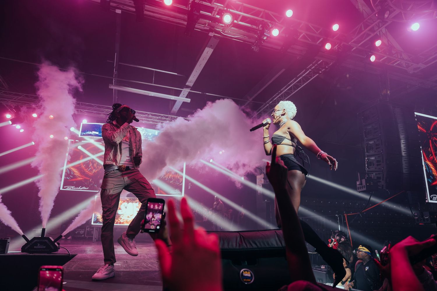 Two artiste performing on stage with pink smoke effects at an energetic live concert.