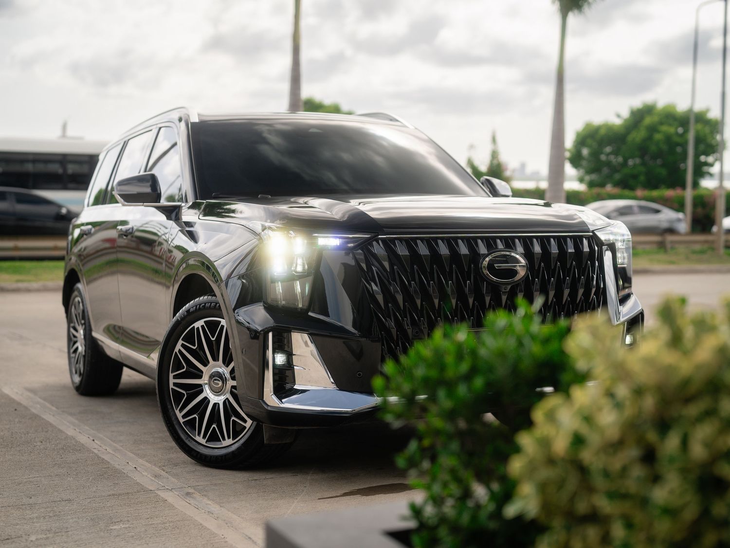 Sleek black luxury SUV with LED headlights parked in a lot surrounded by tropical greenery.