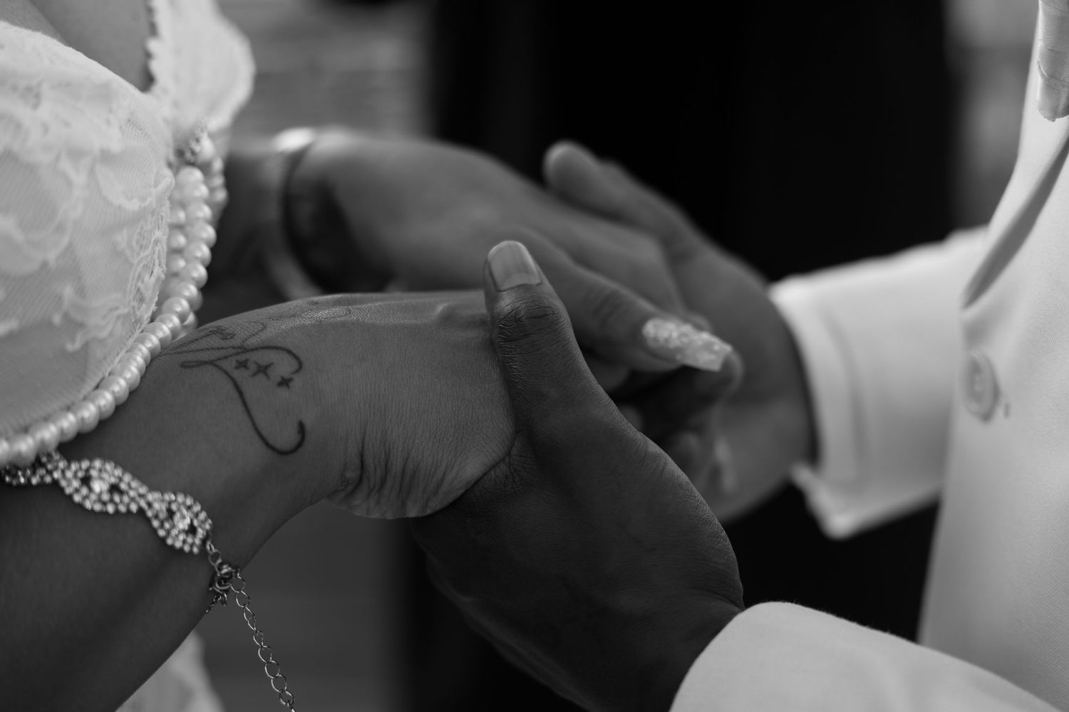 Close-up black and white photo of groom placing wedding ring on bride's hand during ceremony.