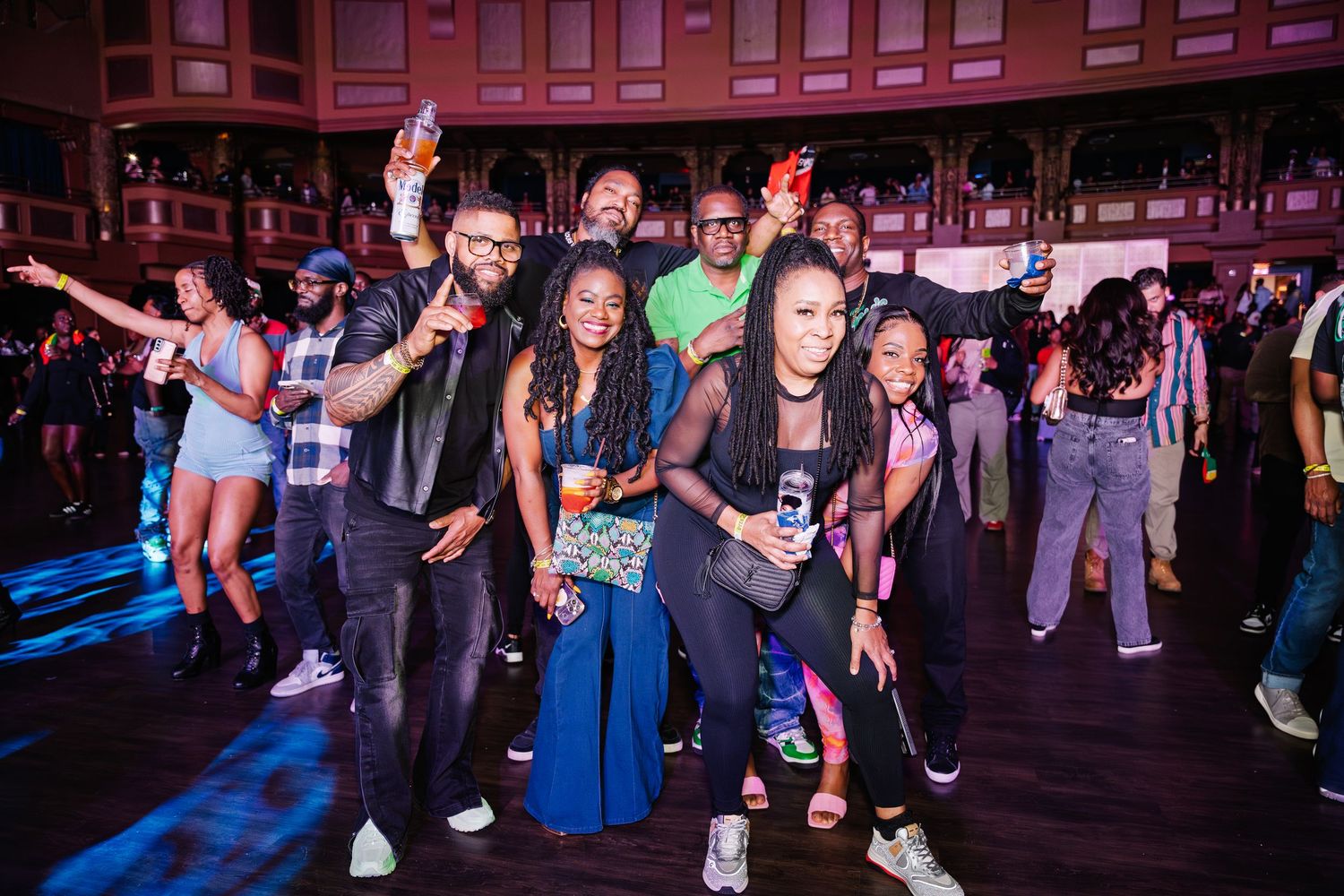 A lively group of people posing and dancing together at a vibrant indoor concert event.
