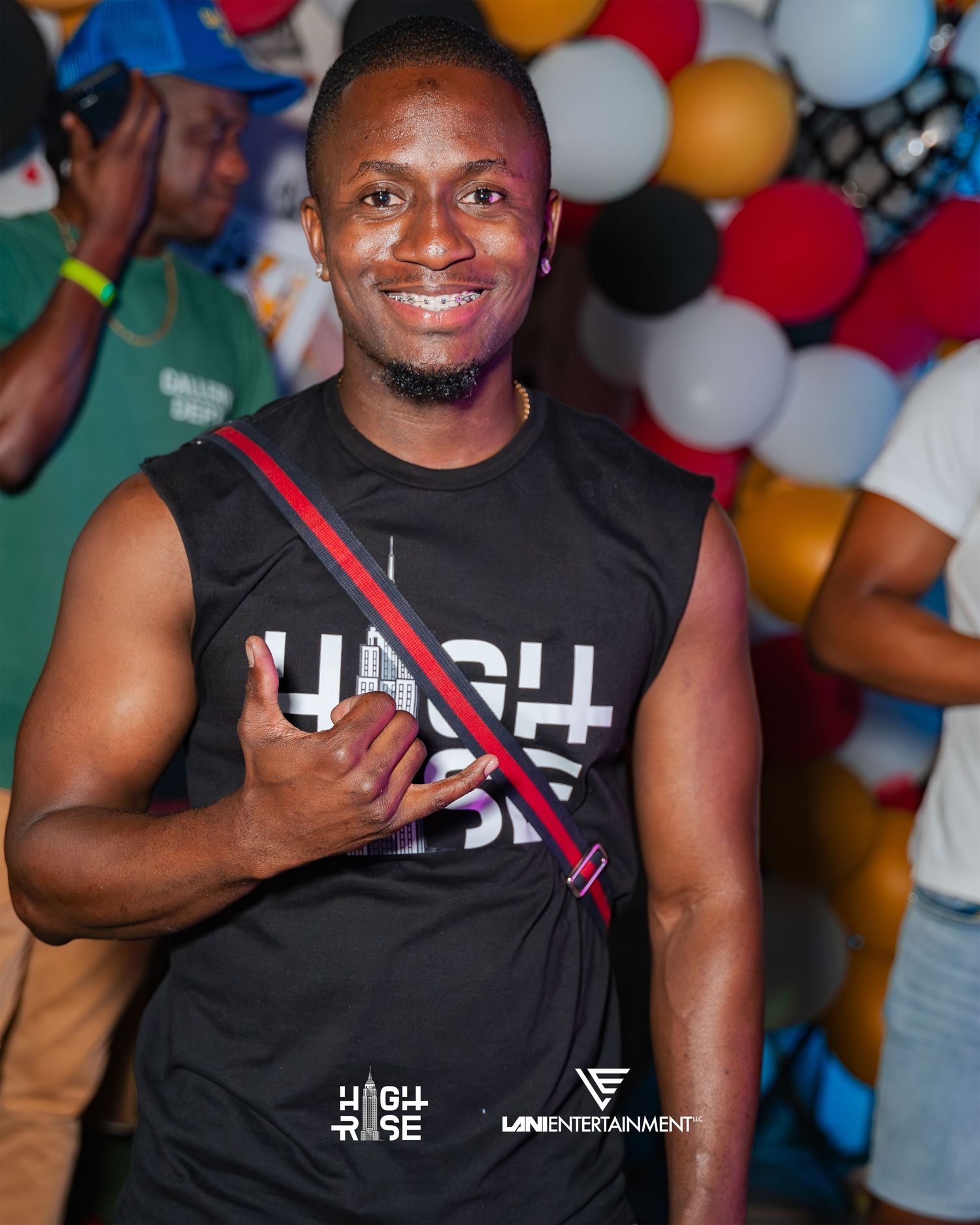 A smiling man wearing a black High Rise sleeveless shirt poses in front of colorful balloons.