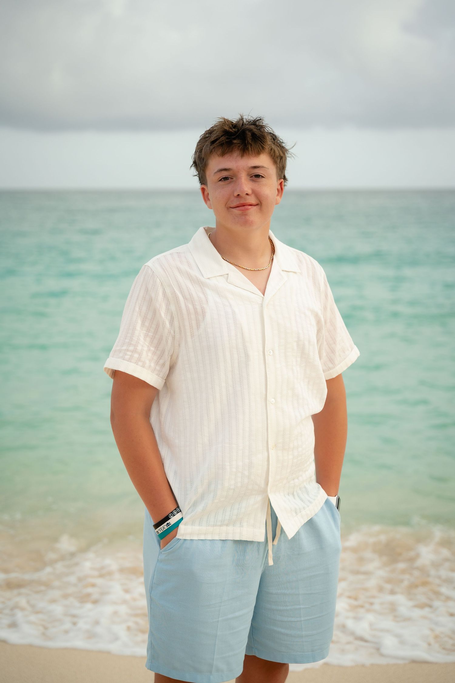 Teenage boy in white shirt and blue shorts standing on a tropical beach.