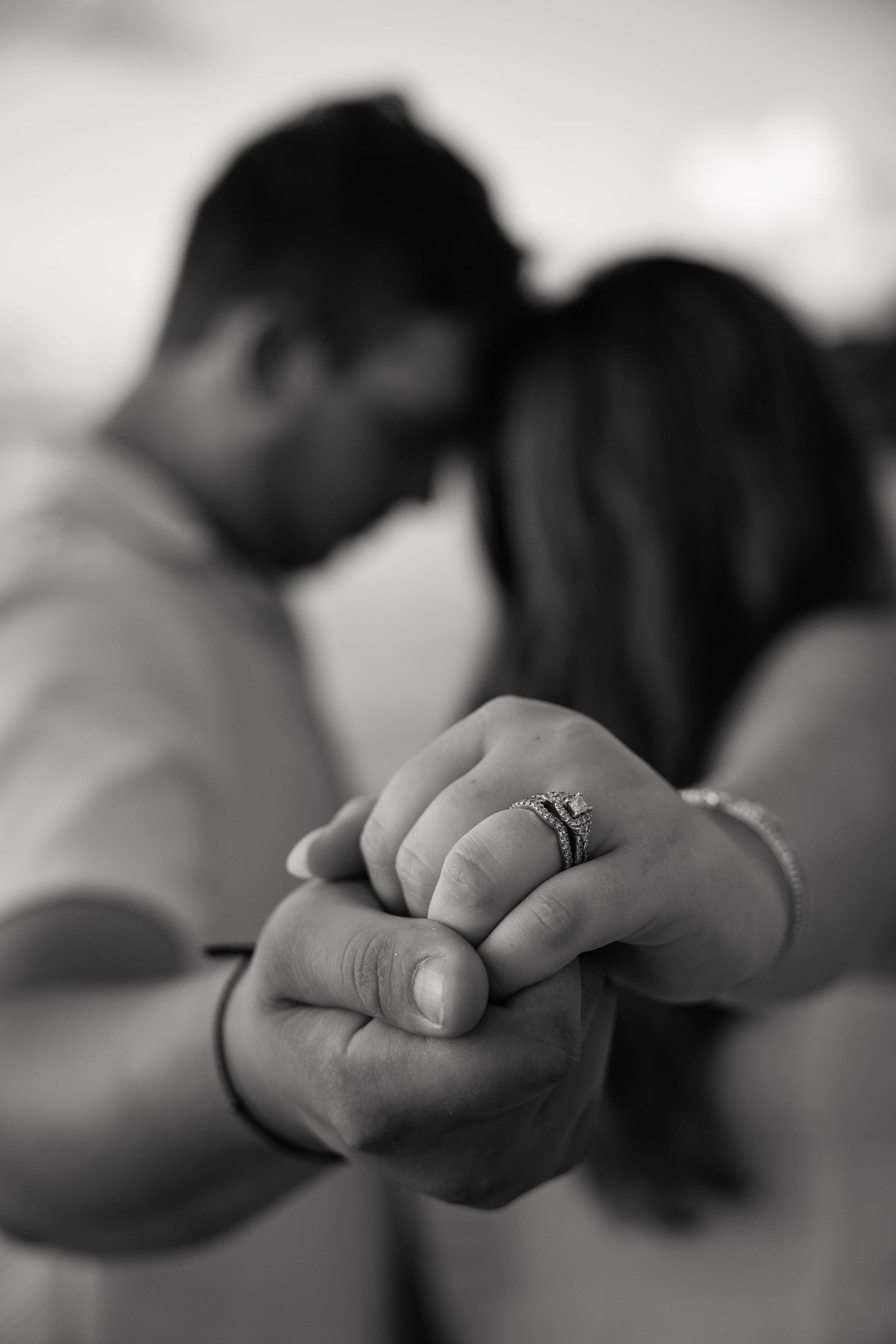 Black and white photo of couple holding hands with engagement ring in foreground.