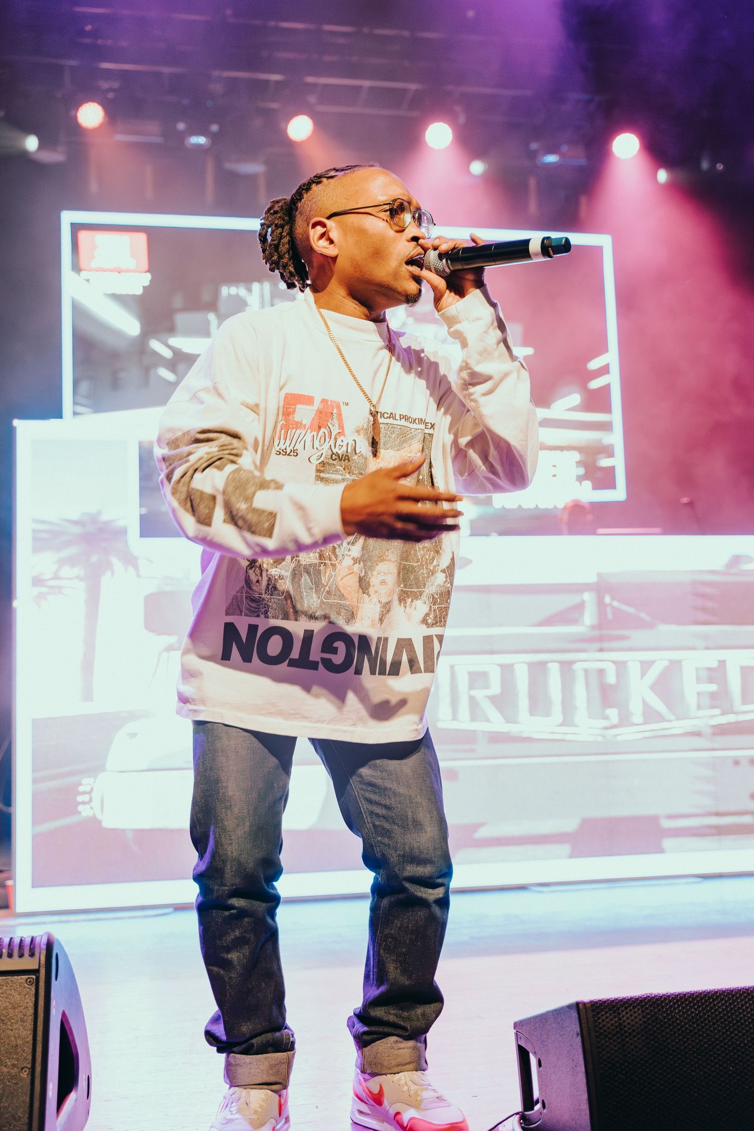 Male Soca artist performs on stage wearing graphic sweatshirt holding microphone at concert.
