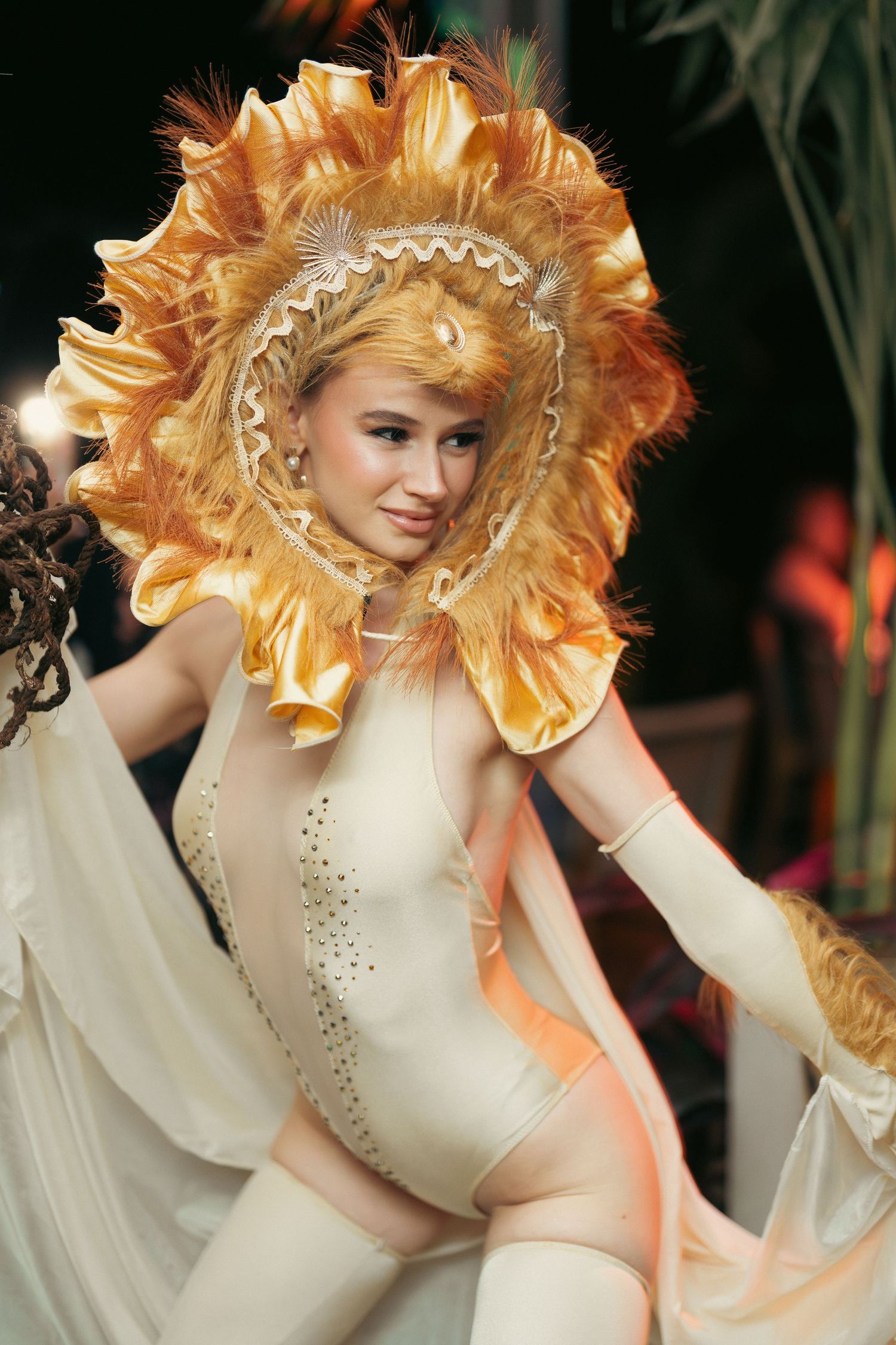 Performer in elegant sunflower costume with feathered headdress and cream bodysuit on stage.
