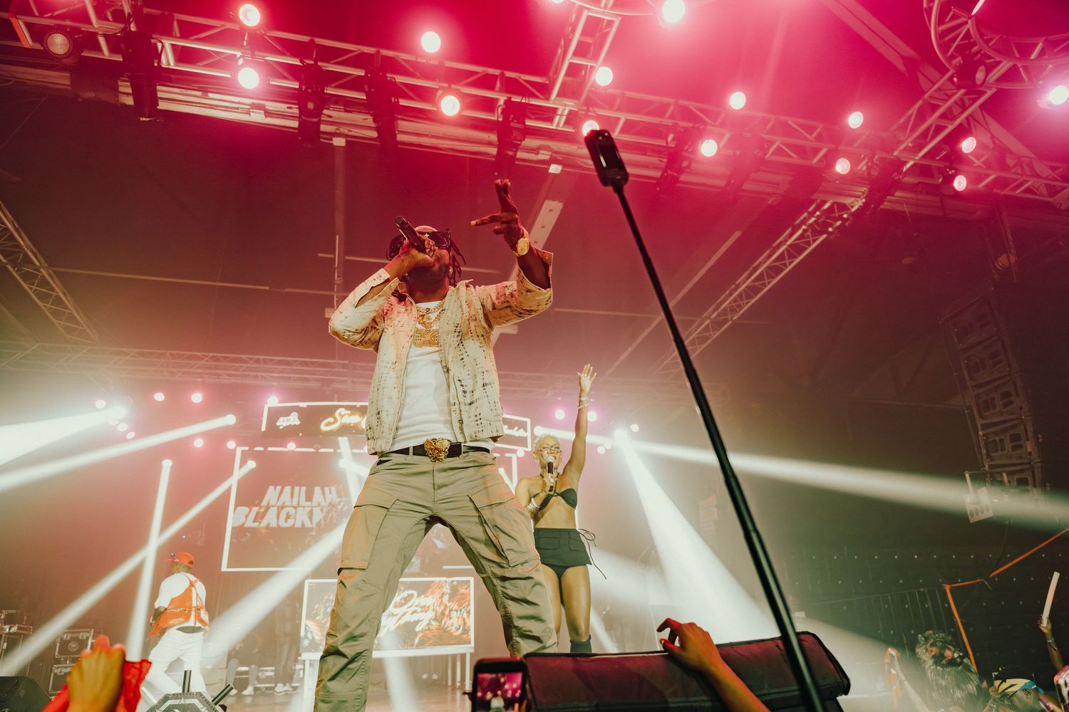 Male artiste performing energetically on stage under red concert lights before a large crowd.