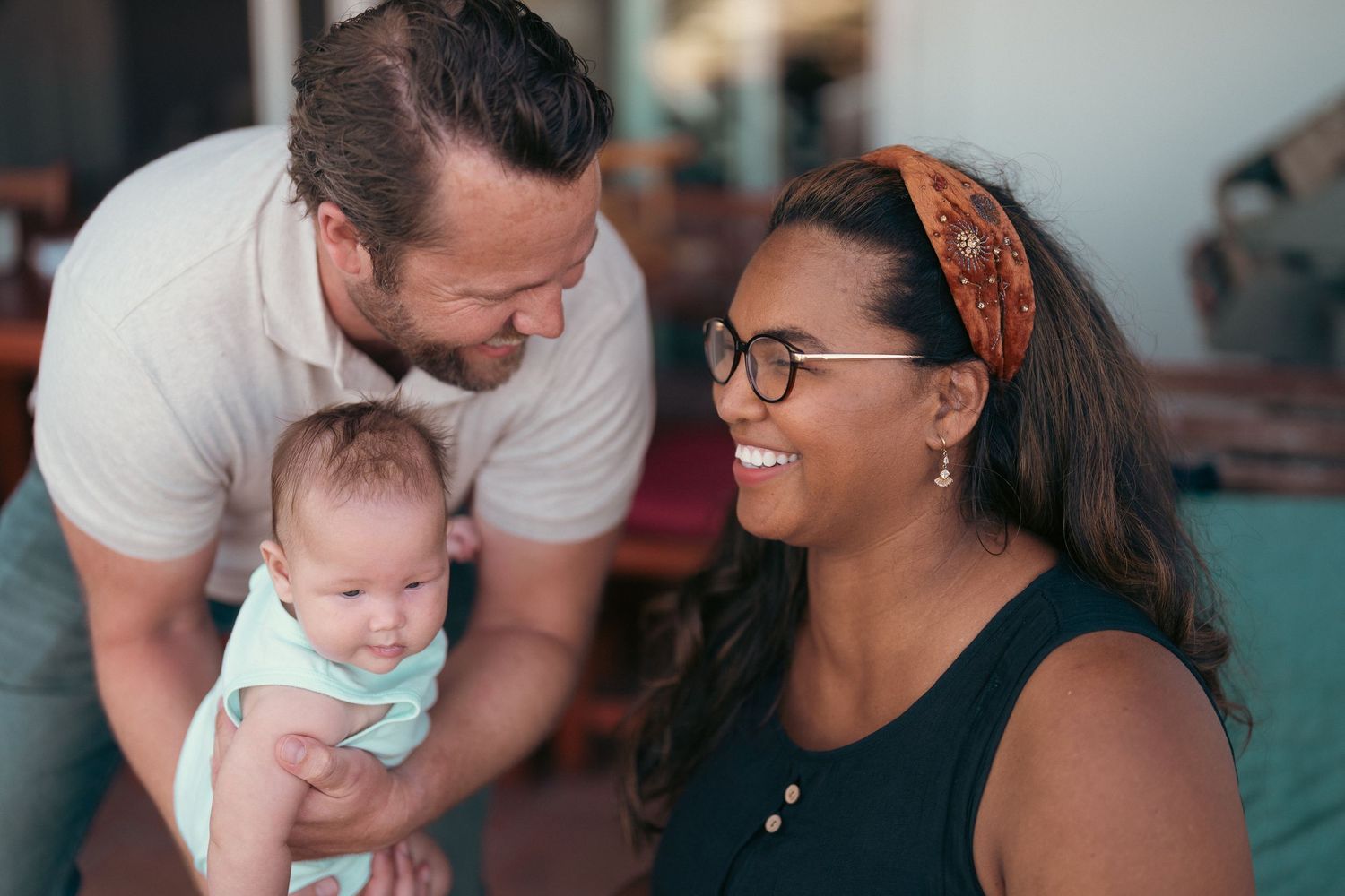 Couple smiling at adorable baby in bright outdoor setting.