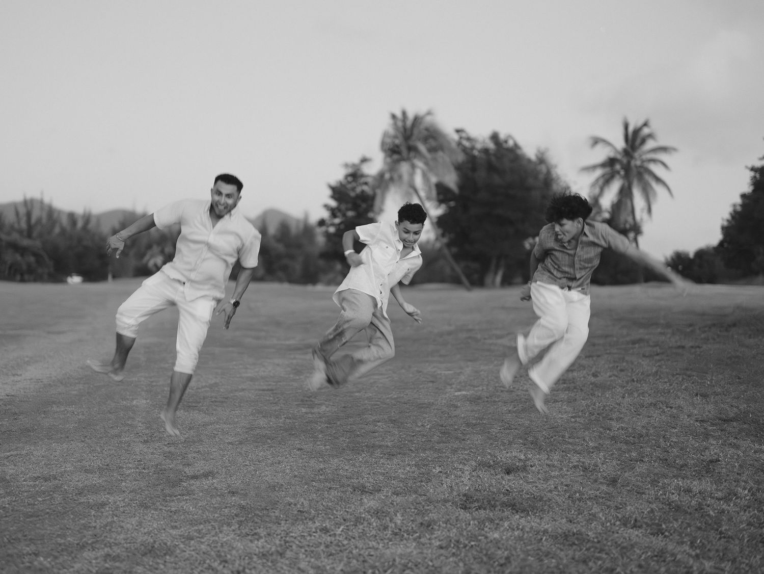 Black and white photo of three people jumping playfully on a grassy field.