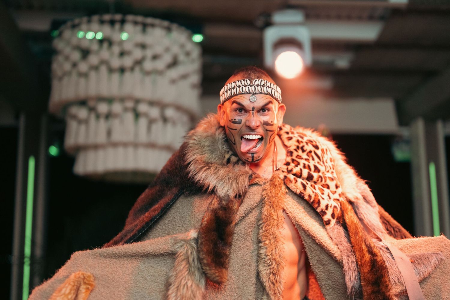 Male performer in tribal fur costume with face paint on a lit stage.