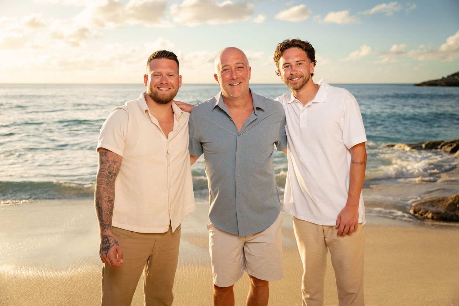 Three men smiling together on a tropical beach at golden sunset.