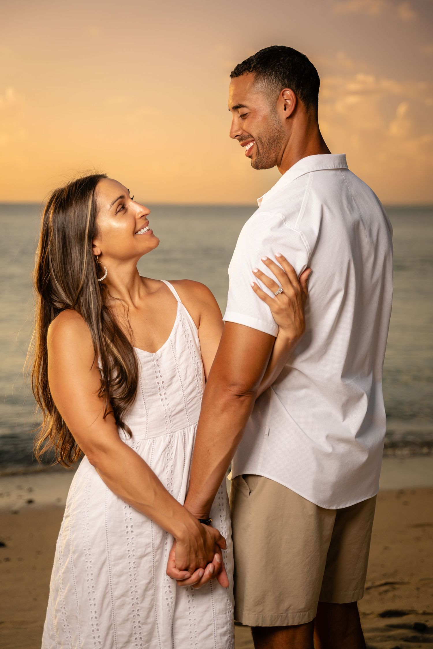 Happy couple holding hands and smiling at each other on beach during sunset.