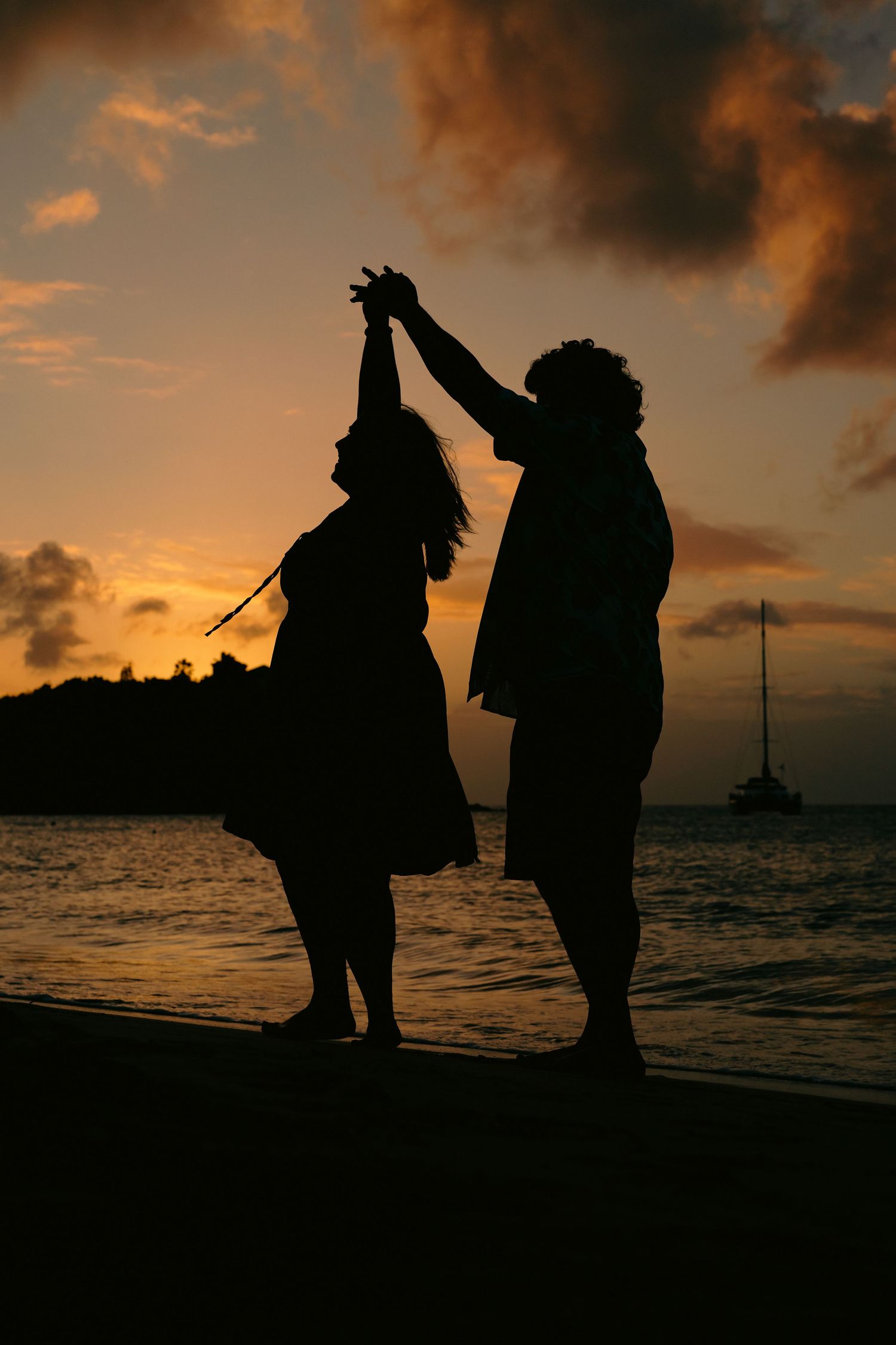 Romantic couple silhouette dancing on beach at vibrant orange sunset with sailboat.