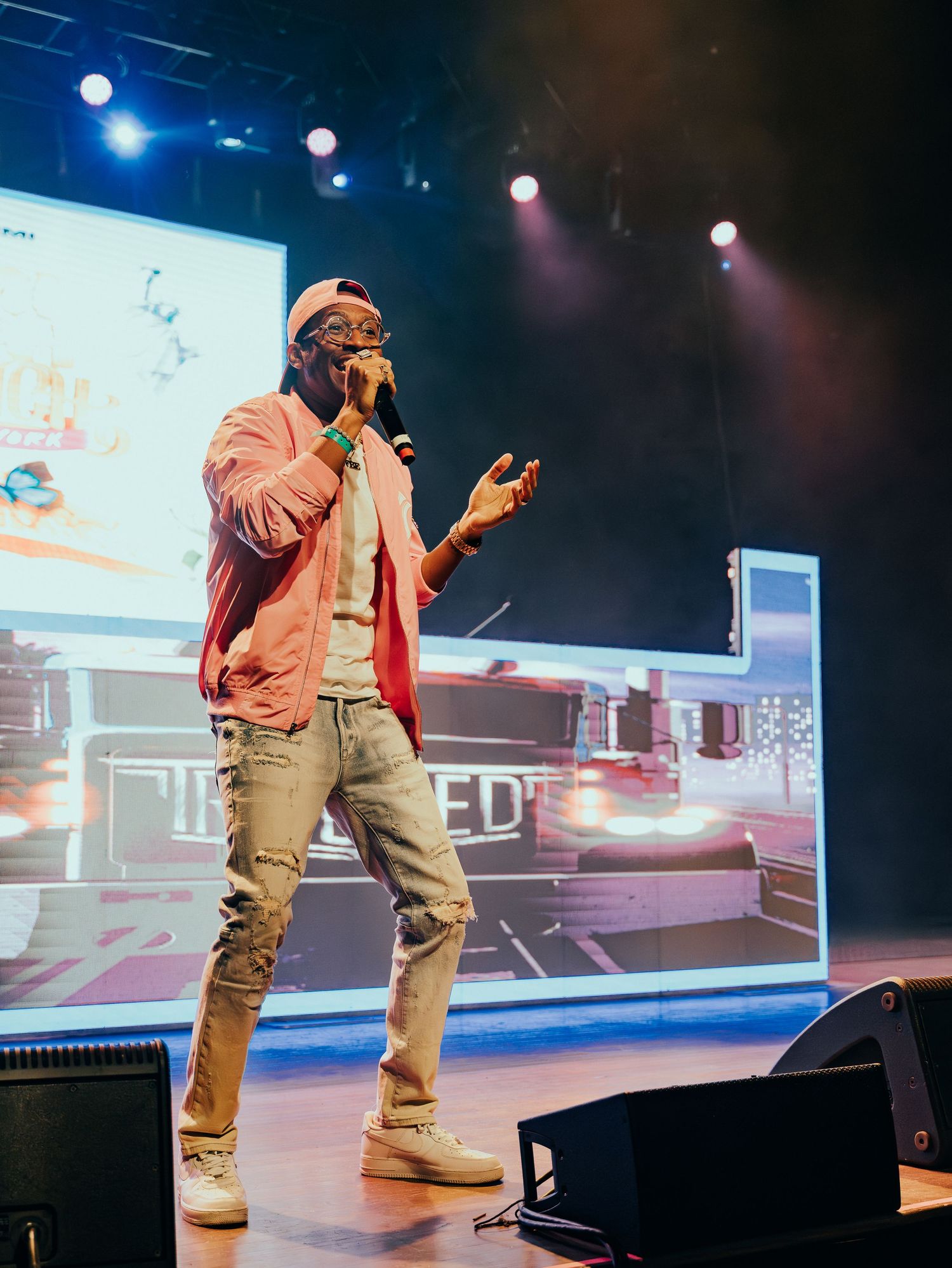 Male artist in pink jacket and ripped jeans performing on stage at a live music event.