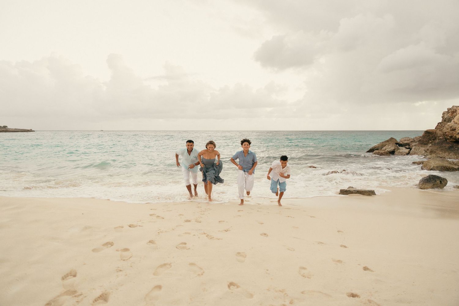 Family of four running joyfully along a sandy beach with ocean waves.