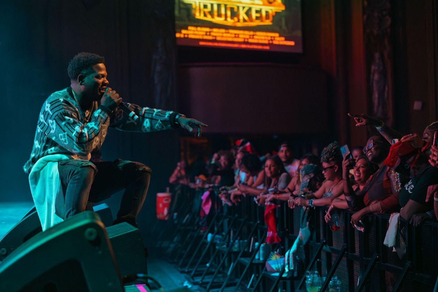 Performer engages crowd at Rucked venue, leaning toward fans during energetic live concert.