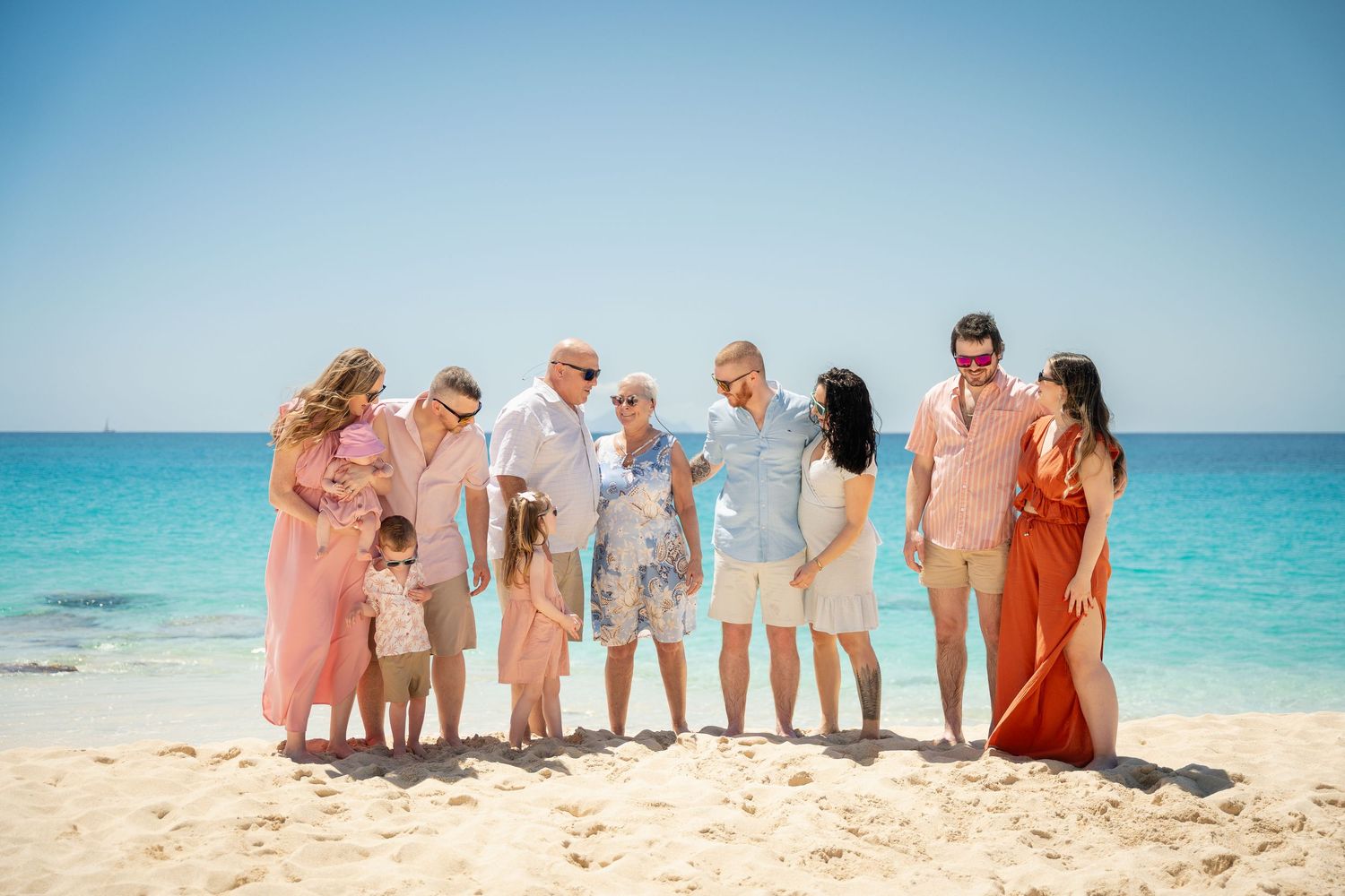 Large multigenerational family gathered together on a bright sunny white sand beach.