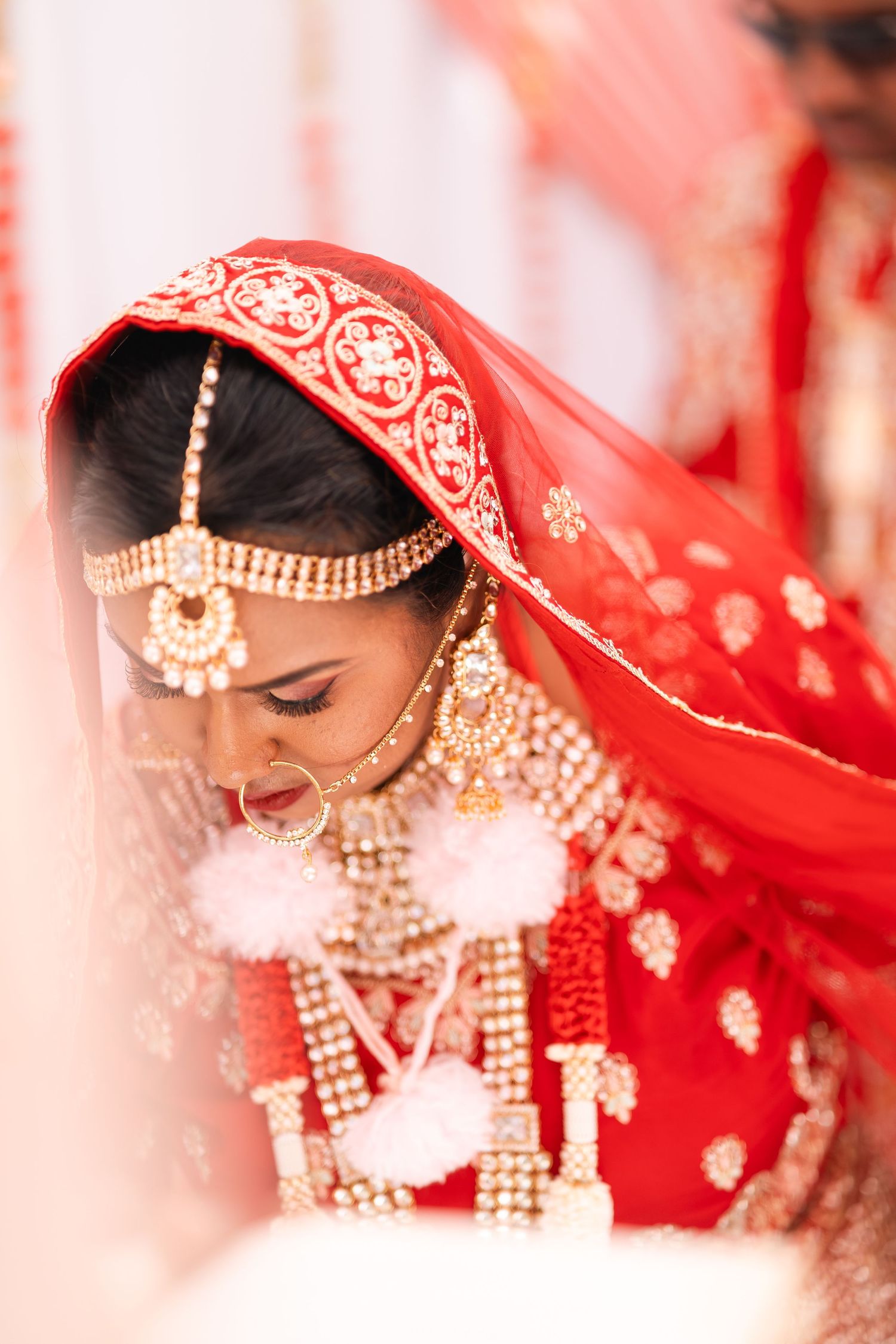 Close-up portrait of Indian bride in red lehenga adorned with gold jewelry and maang tikka.