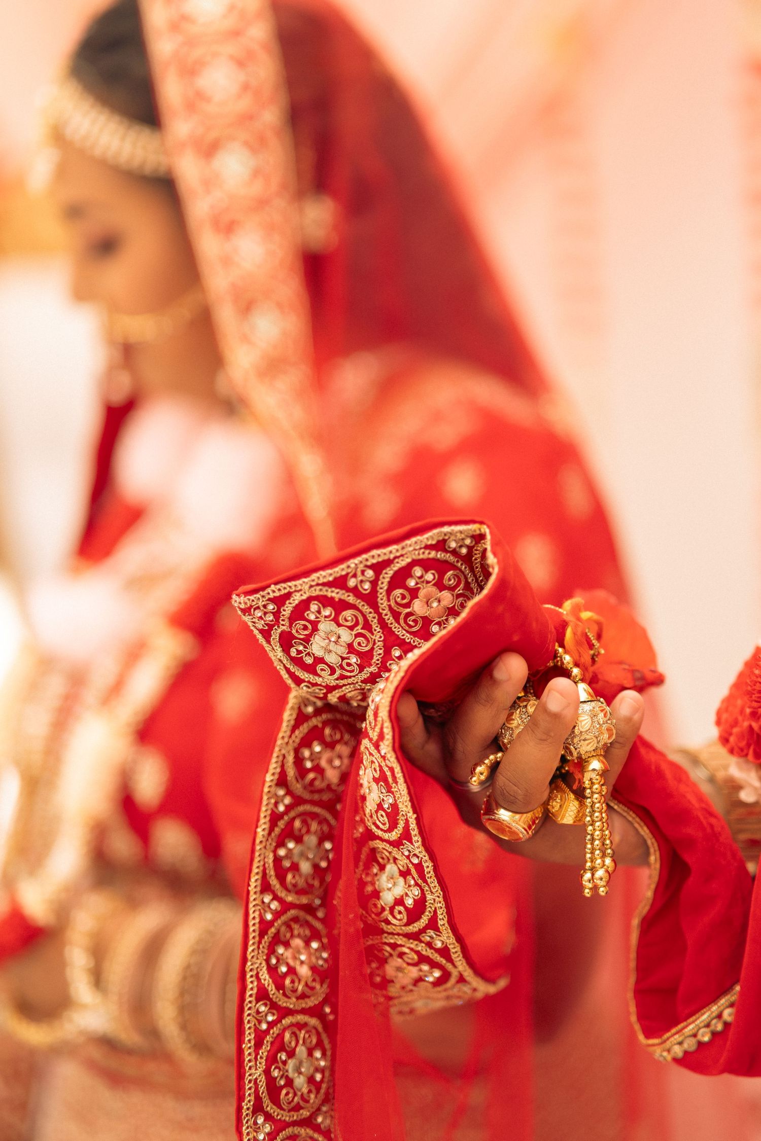 Close-up of Indian bride and groom hands tied together with red dupatta during wedding ritual.