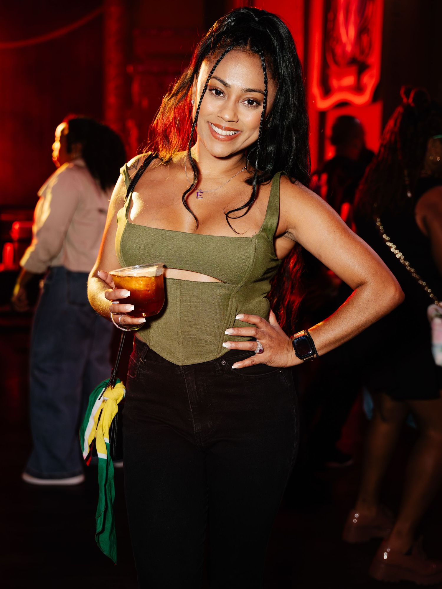 Smiling woman holding a cocktail at an indoor music event under red lights.