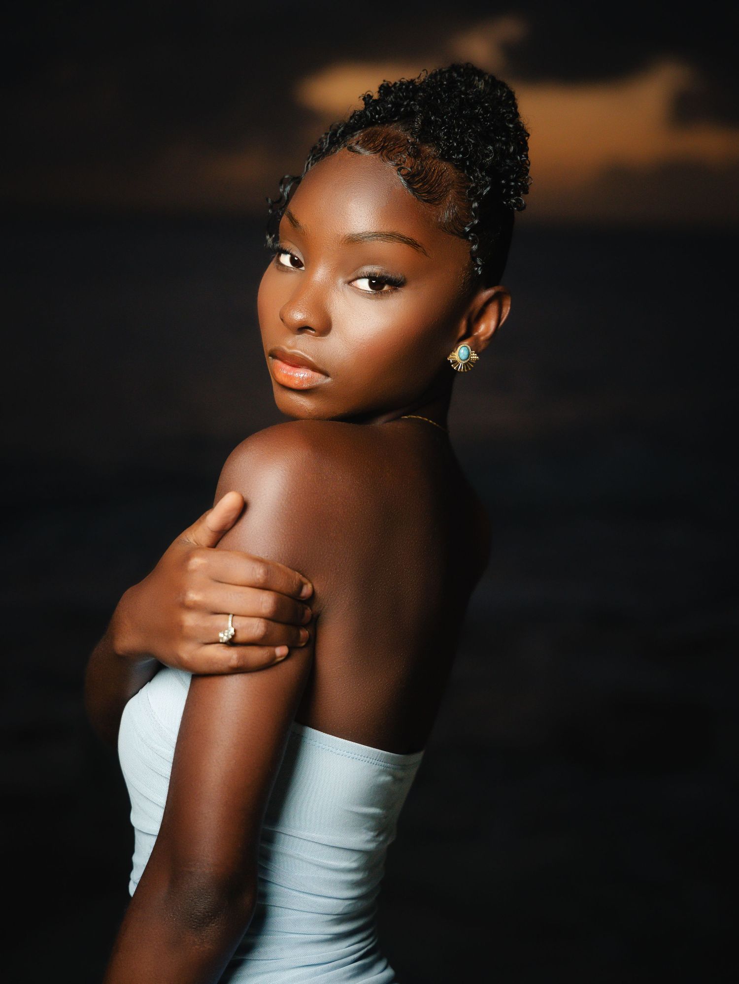 Elegant young Black woman in strapless light blue dress posing gracefully against a dark ocean backdrop.