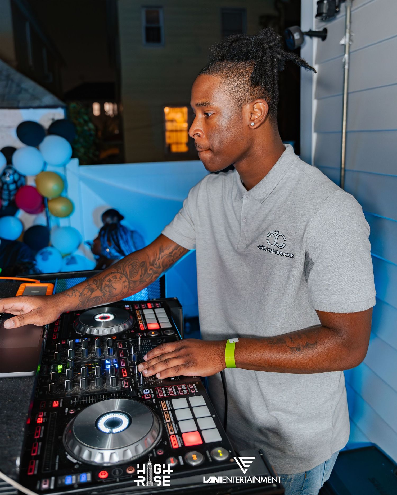 DJ performing at an outdoor party event using a Pioneer DJ controller with tattoos visible on his arm.