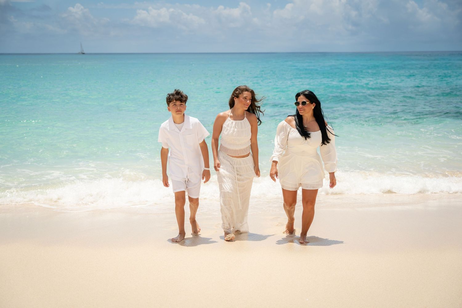 Three people in white outfits walk along a tropical white sand beach together.