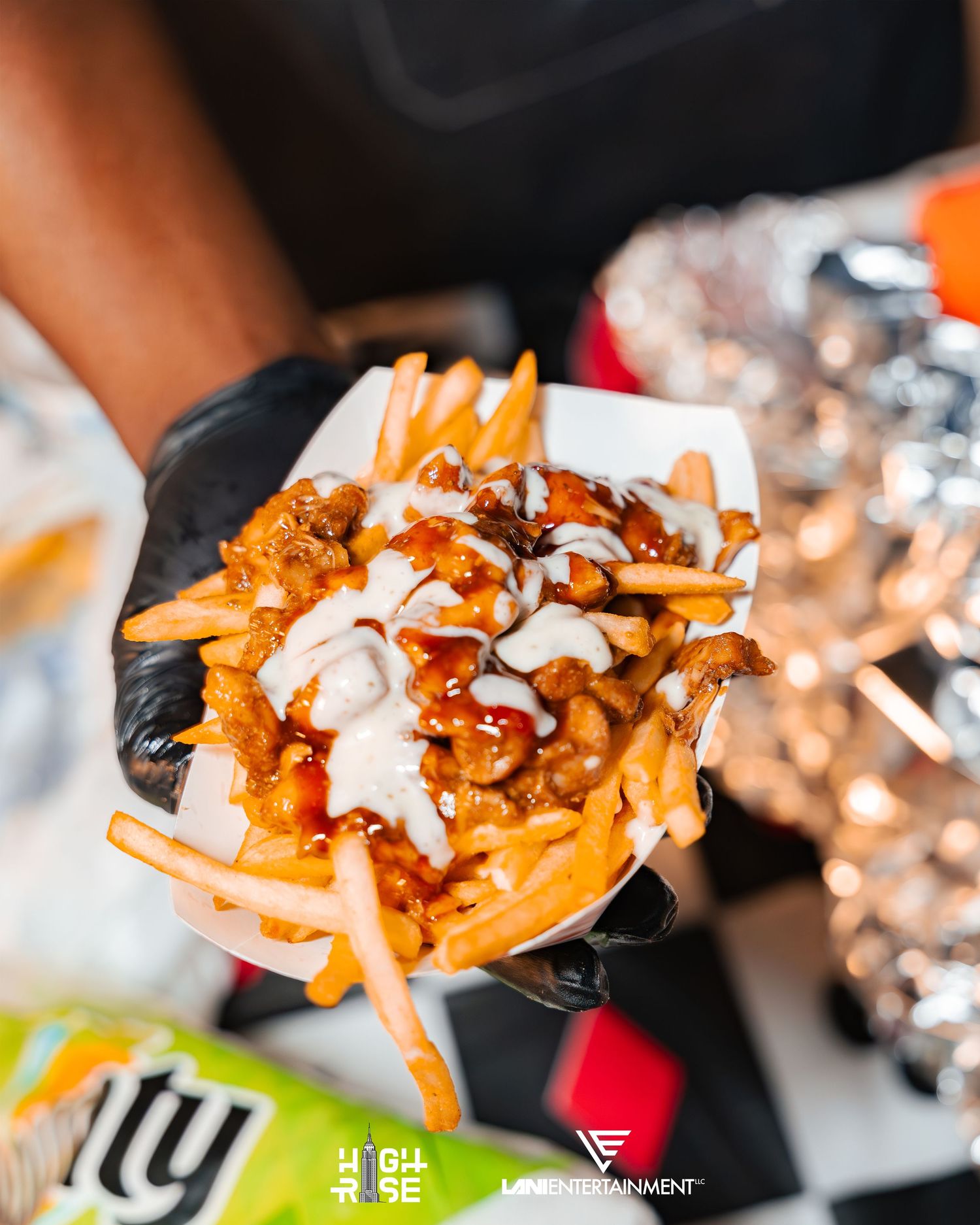 Loaded chili cheese fries topped with white sauce served in a paper container at a food event.