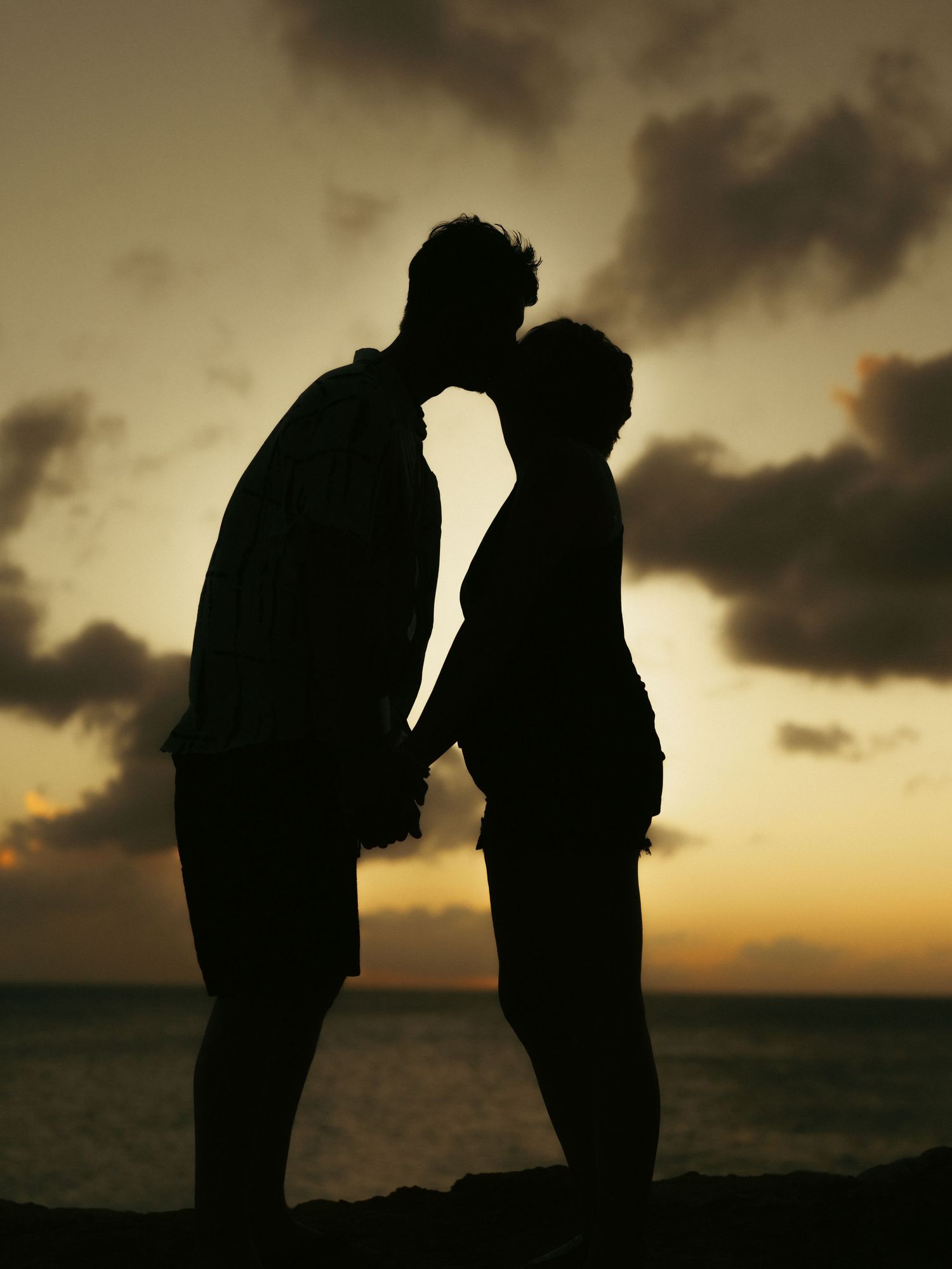 Romantic silhouette of couple kissing at sunset by the ocean.