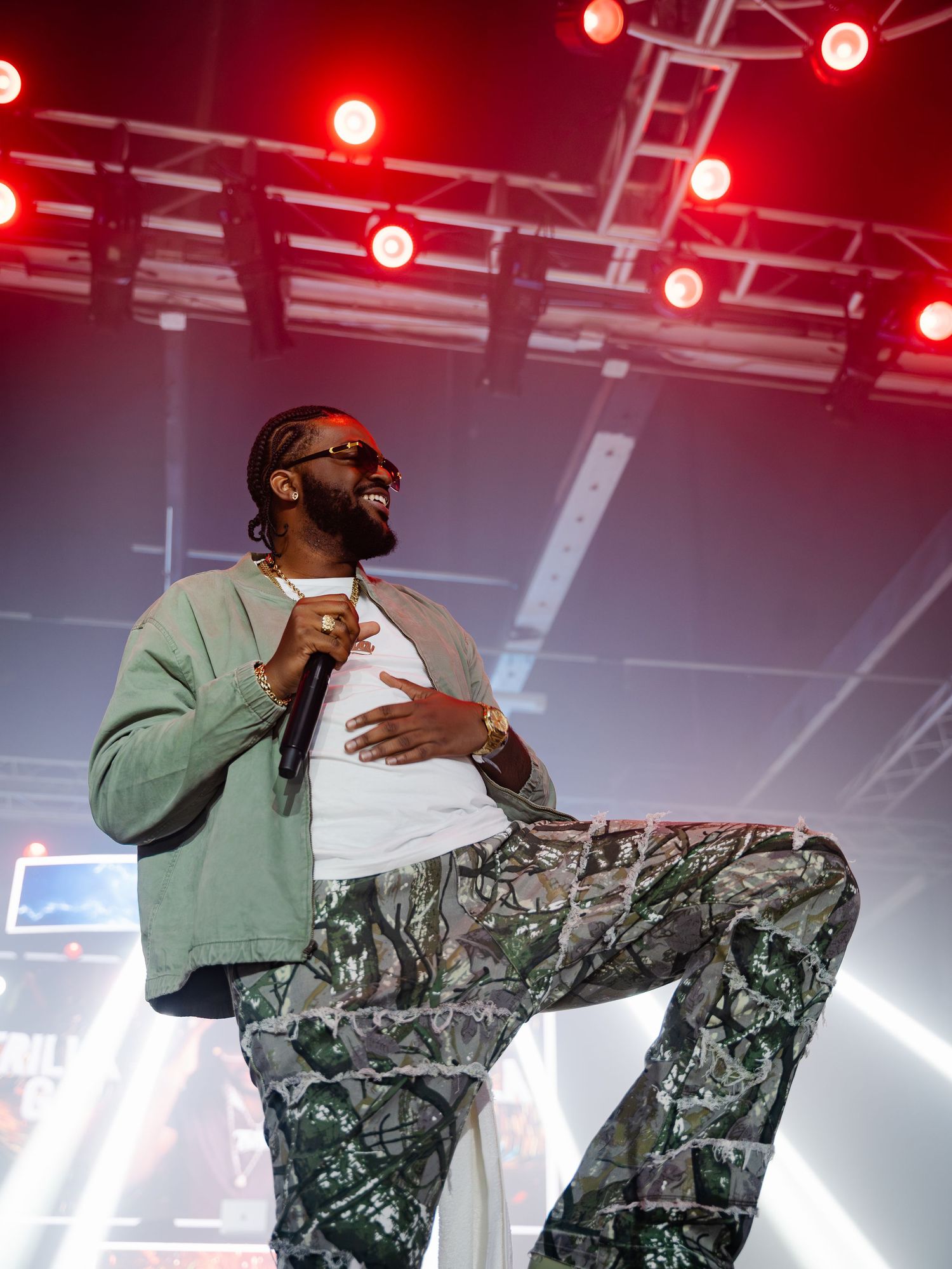 Male performer in camo pants and gray jacket dancing on a lit stage.