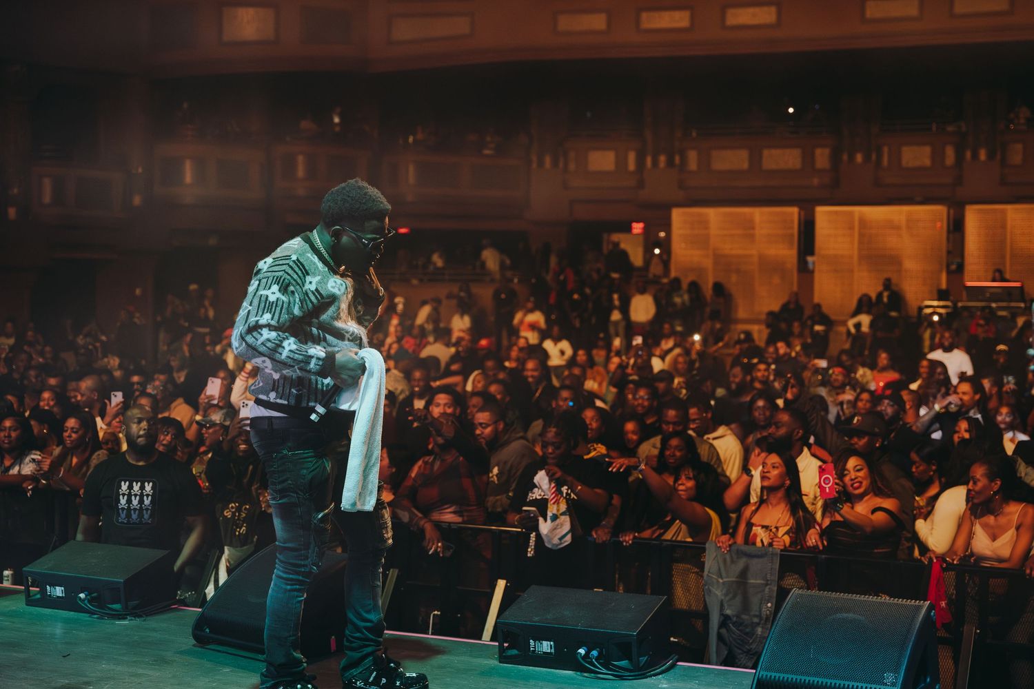 A concert performer standing on stage with their back to a large crowd.