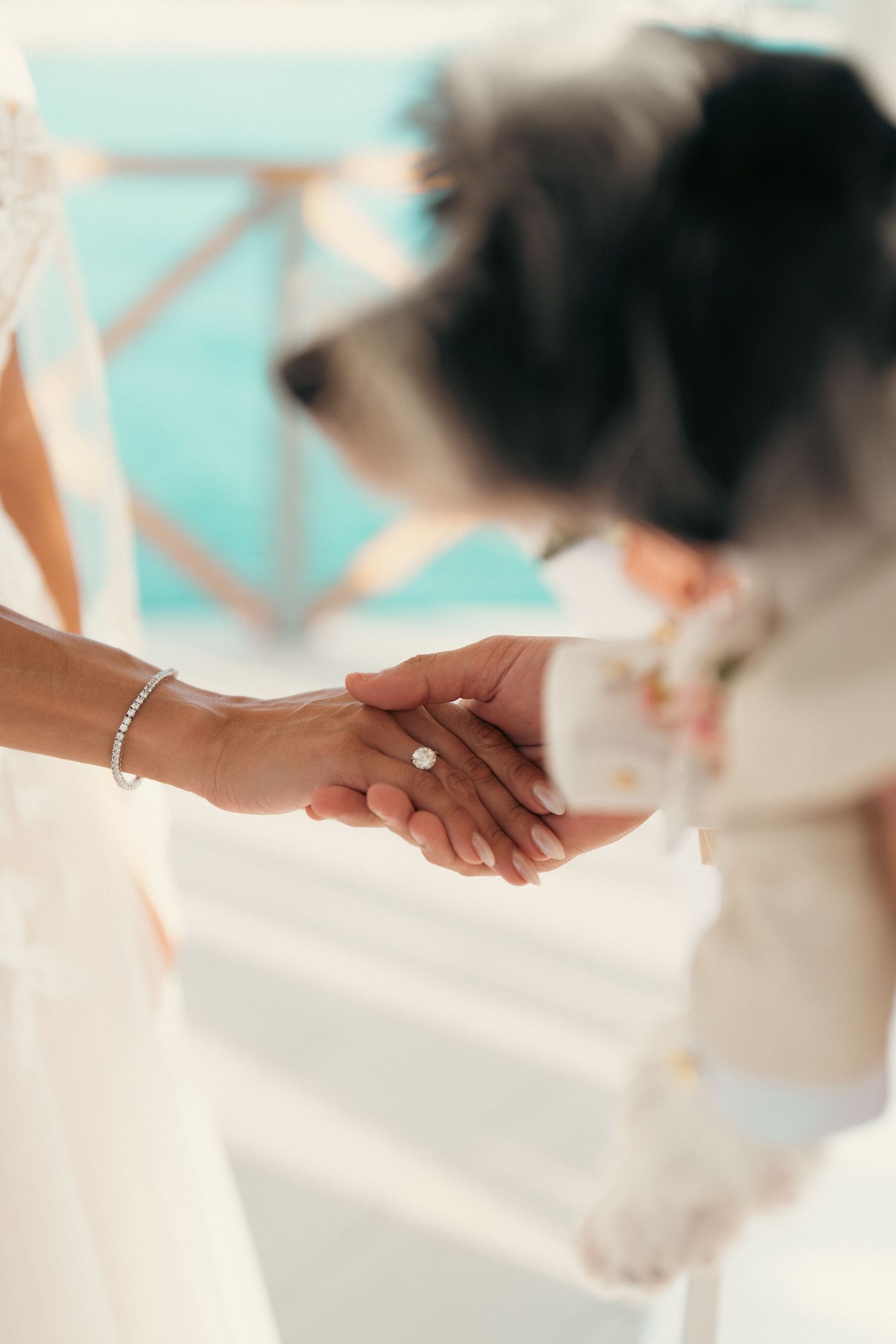 Bride holding an engagement ring while a fluffy dog stands in the background during wedding preparations.