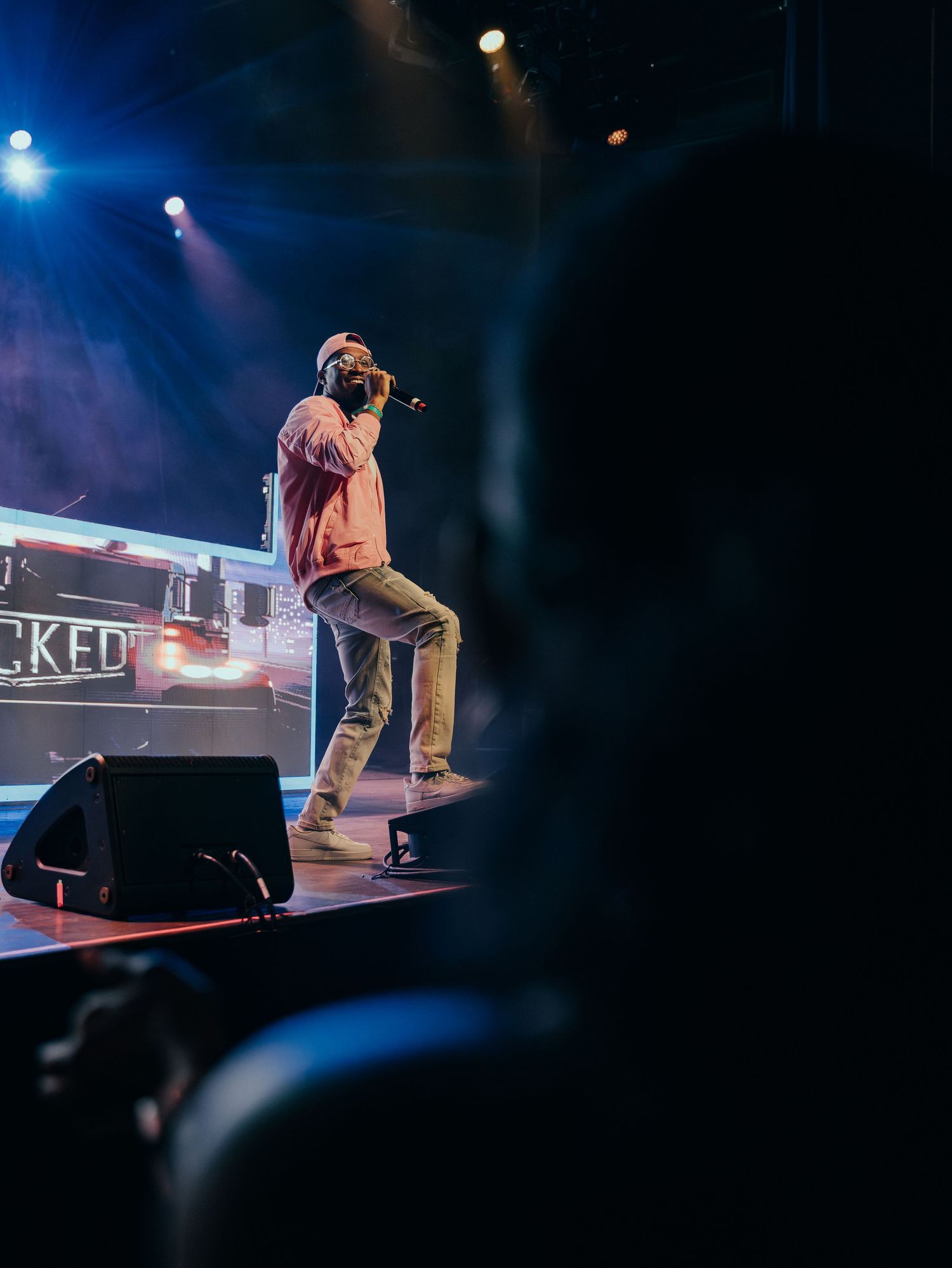 Male performer in pink jacket singing on stage viewed from behind the audience.