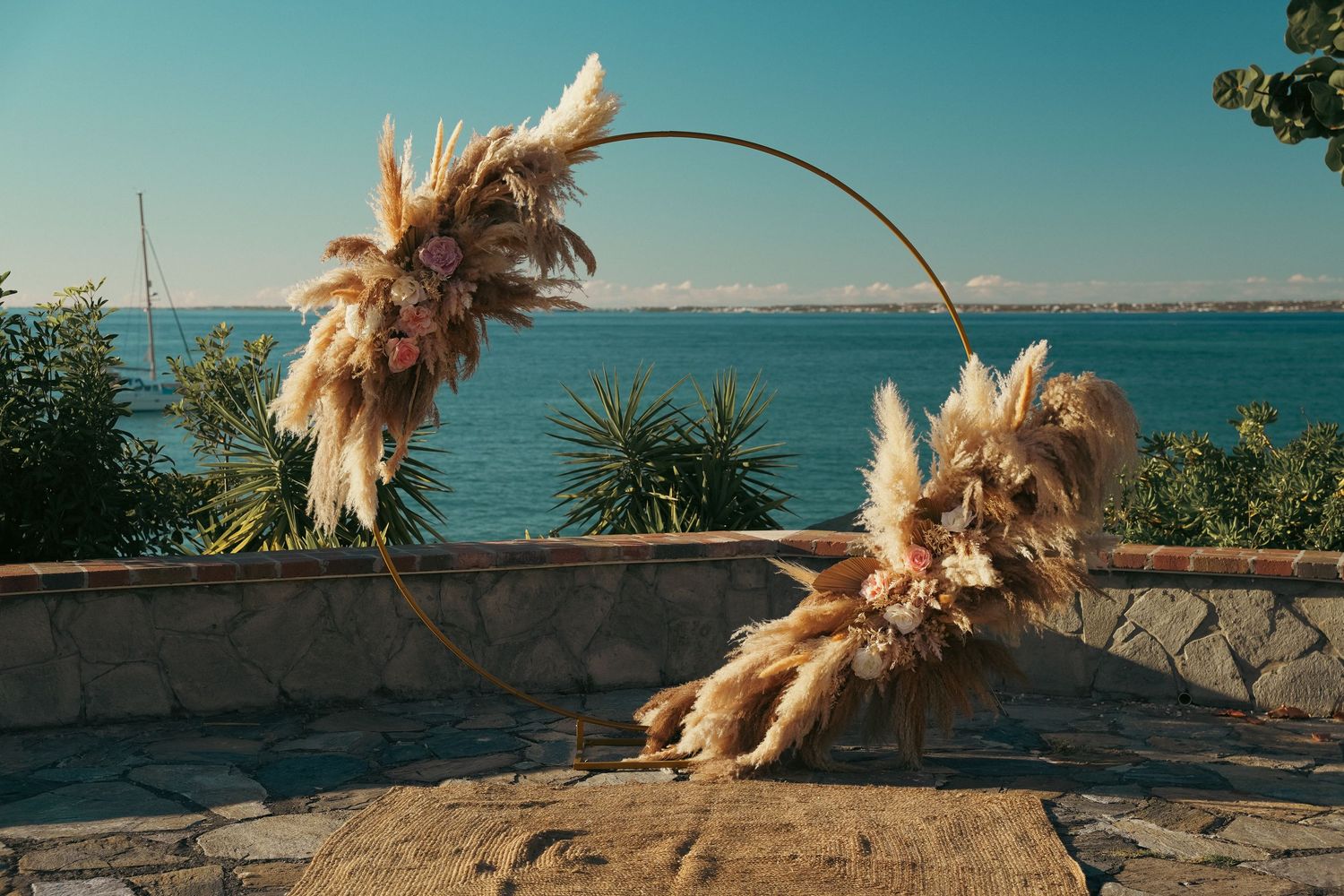 Circular boho wedding arch decorated with pampas grass overlooking a serene ocean view.