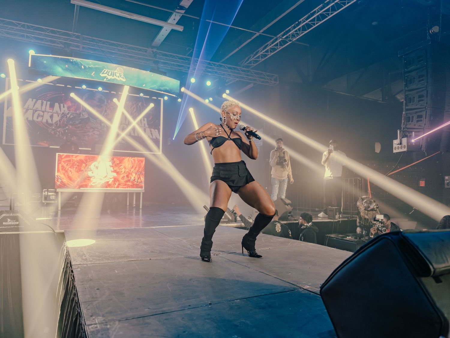 Female artiste in black outfit performs on illuminated stage with laser lights at live music event.