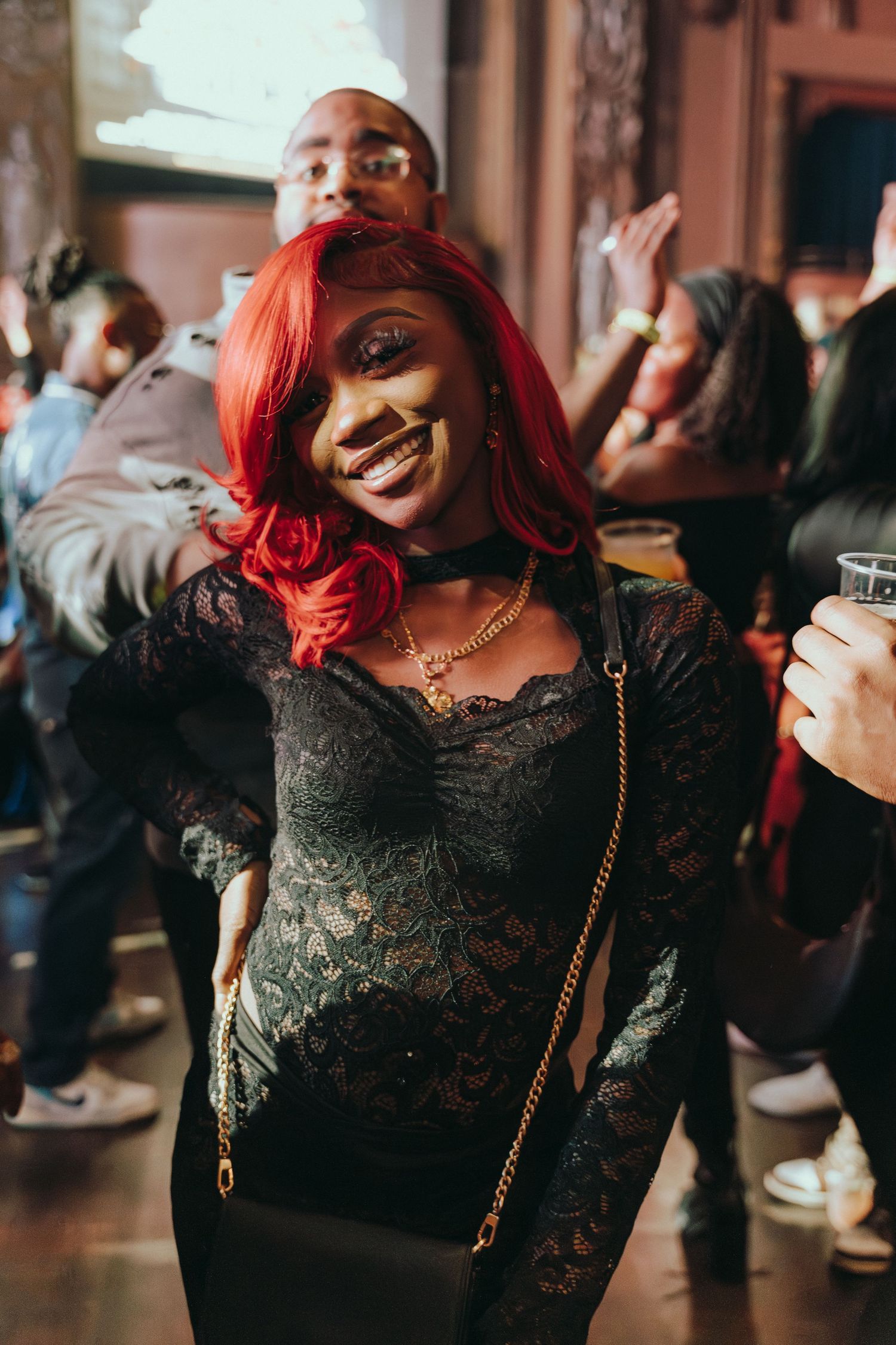 Woman with red hair in black lace dress smiling and dancing at a lively party event.