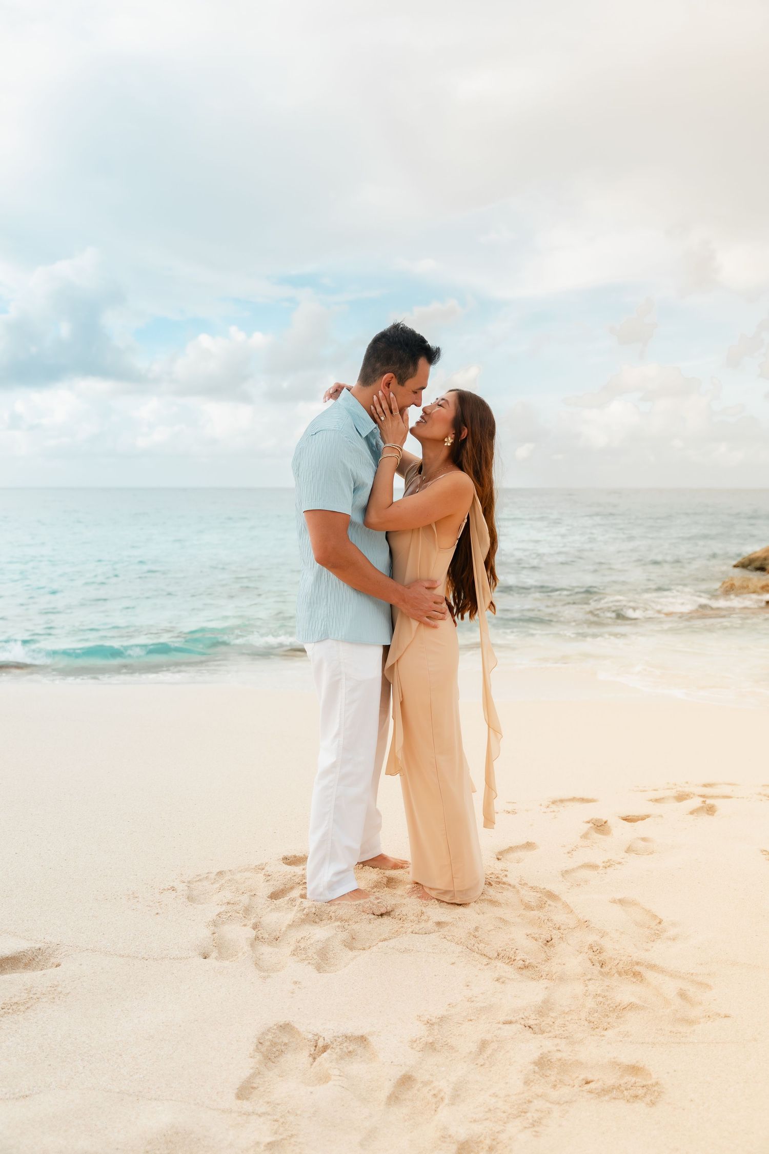 A romantic couple nearly kissing on a white sandy Caribbean beach with turquoise water behind them.