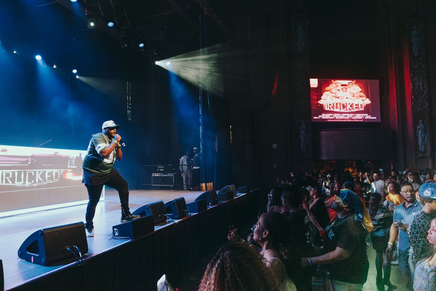 Performer engages with front row crowd on stage at a lively indoor concert venue.