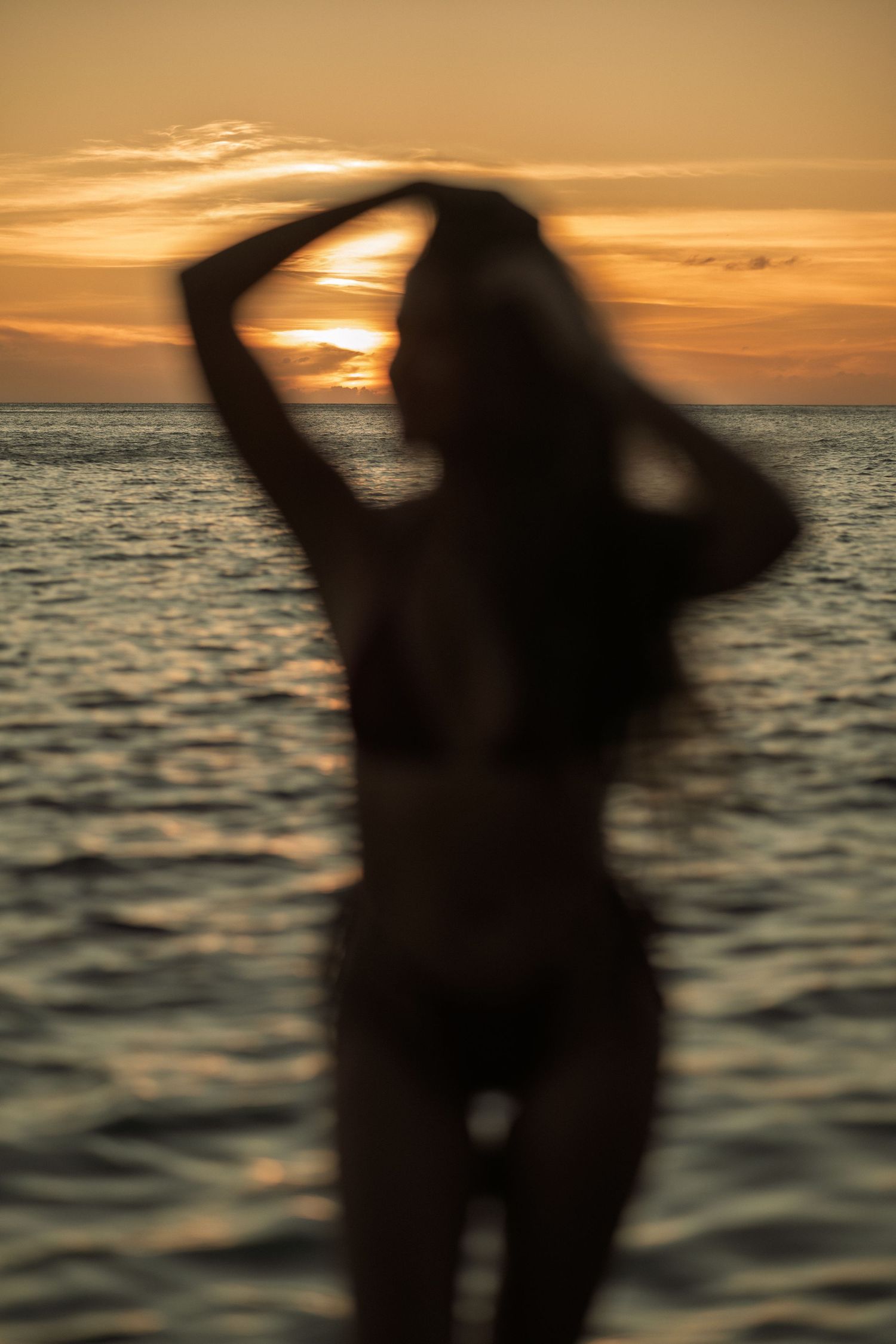Silhouette of a woman in a bikini posing against a stunning golden ocean sunset.