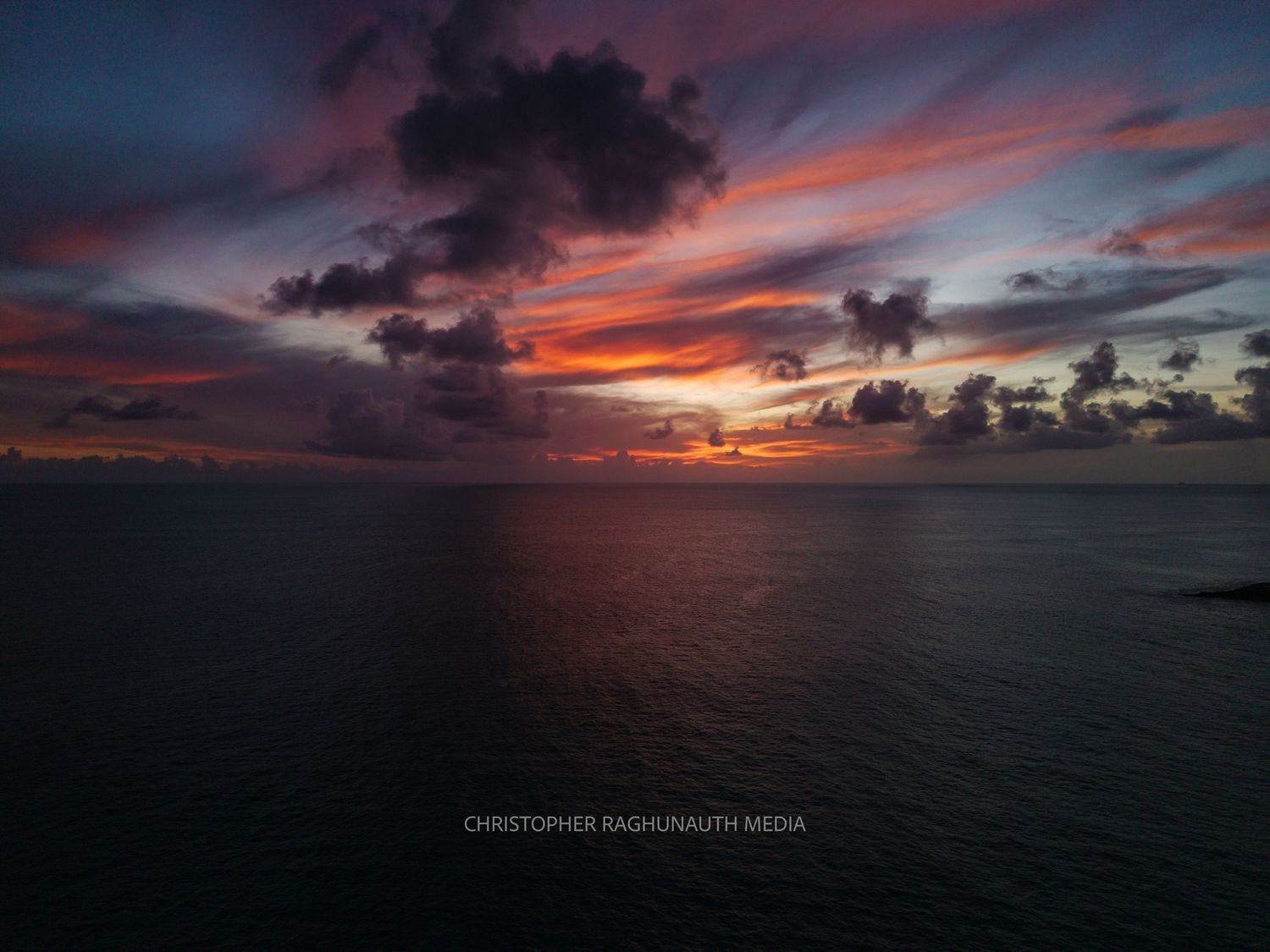 Stunning ocean sunset with vibrant red and purple clouds reflecting over calm dark waters.