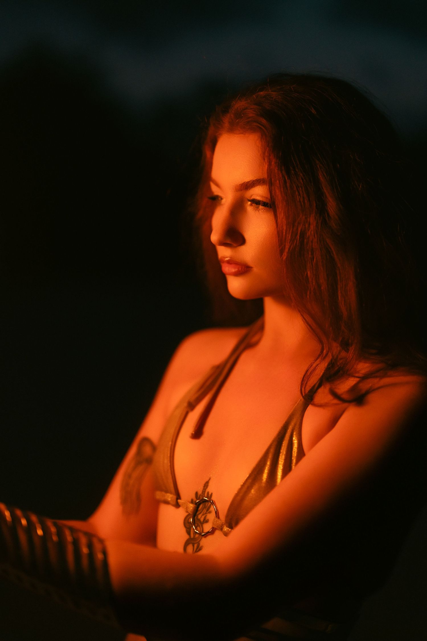 A young woman in a gold bikini is dramatically lit by warm orange light against a dark background.