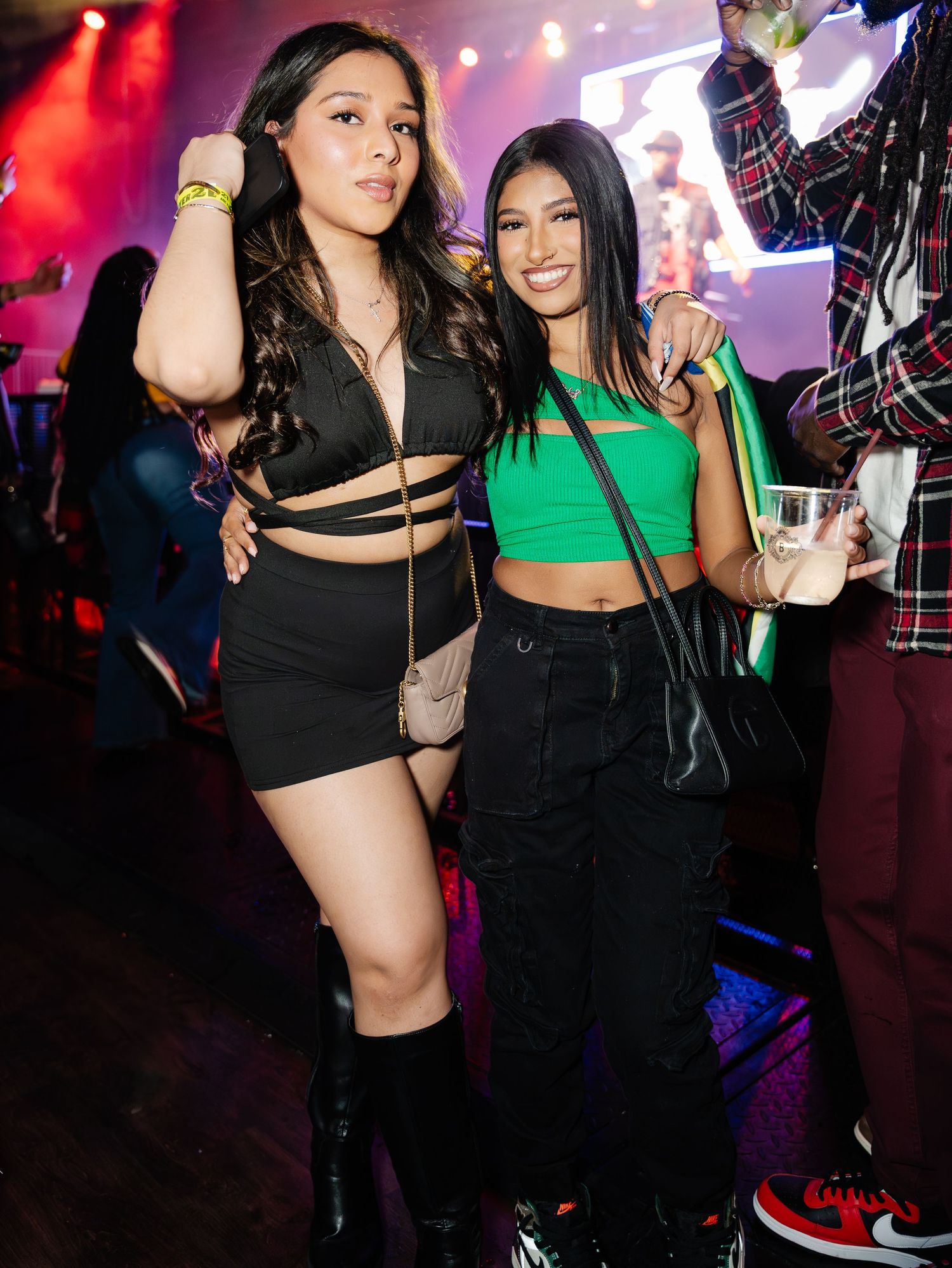 Two young women posing together at a concert venue with colorful lighting.